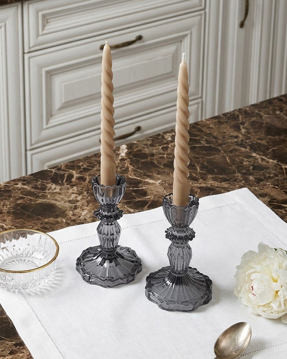 Decorative setup with candlesticks, glass bowl, spoon, and flower on a marble countertop.