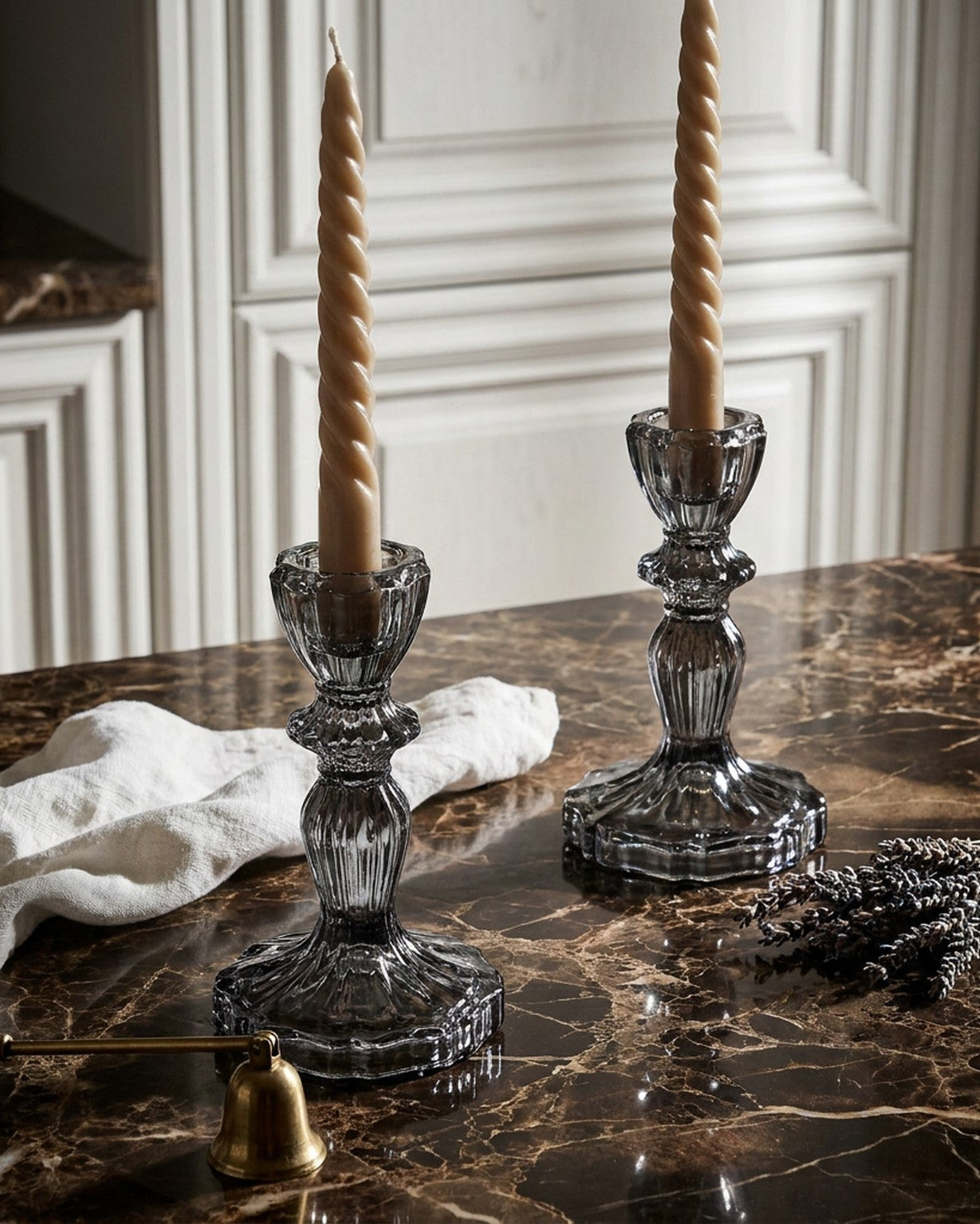 Two crystal candle holders with beige candles on a marble surface.