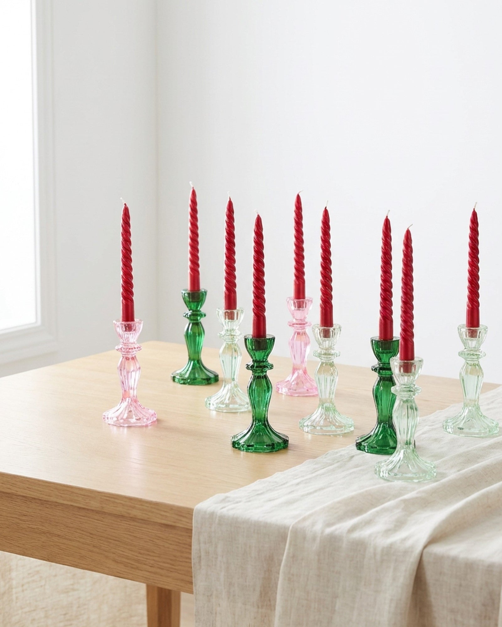 Two green clear glass candleholders on a wooden surface with a red flower in the background.