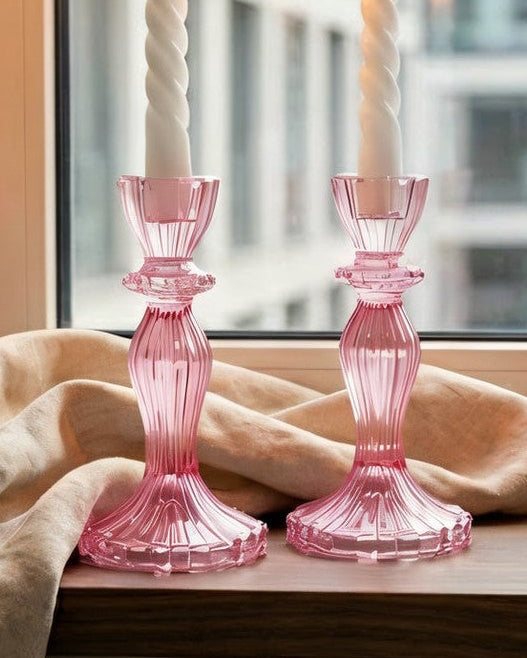 Pink candlesticks on a windowsill with a cityscape view