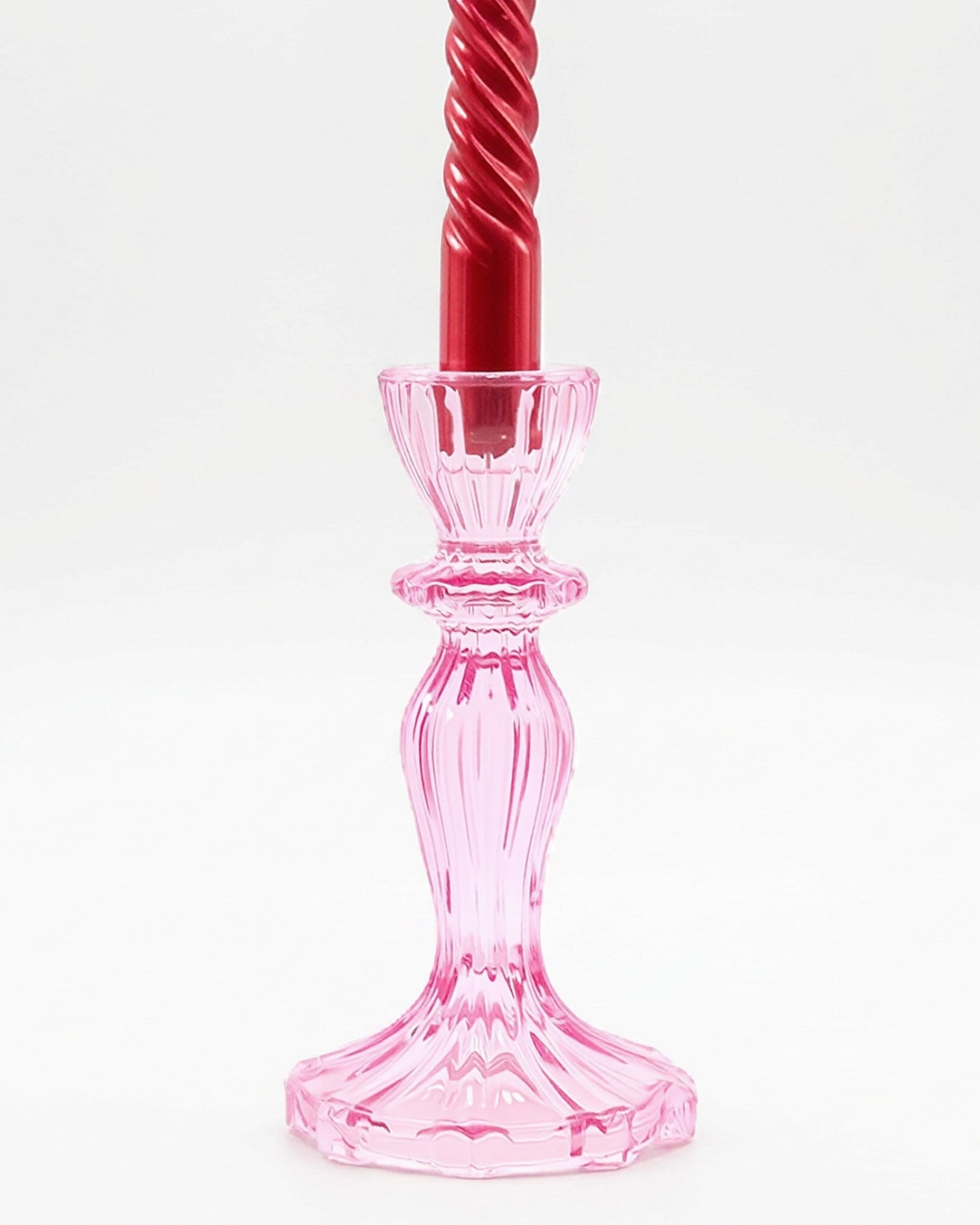 Pink glass candlestick holder with a red candle on a white background