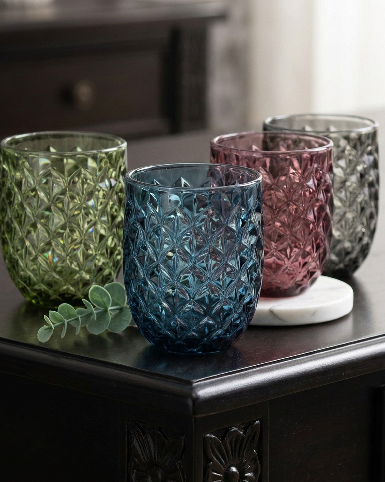 Four textured glass tumblers on a dark surface with a blurred background