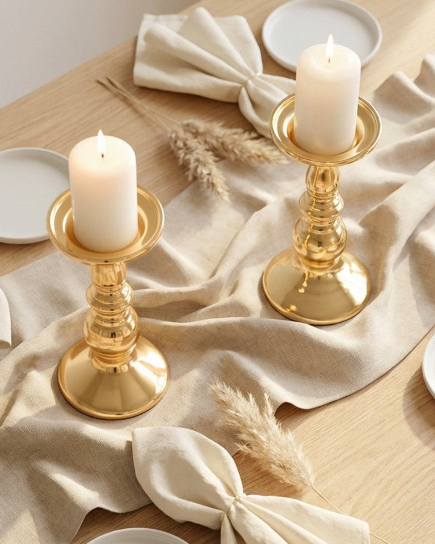 Table setting with gold candle holders, white candles, and beige napkins on a wooden table.