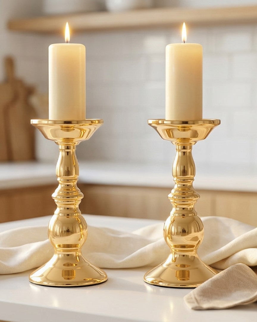 Two gold candle holders with white candles on a kitchen counter.