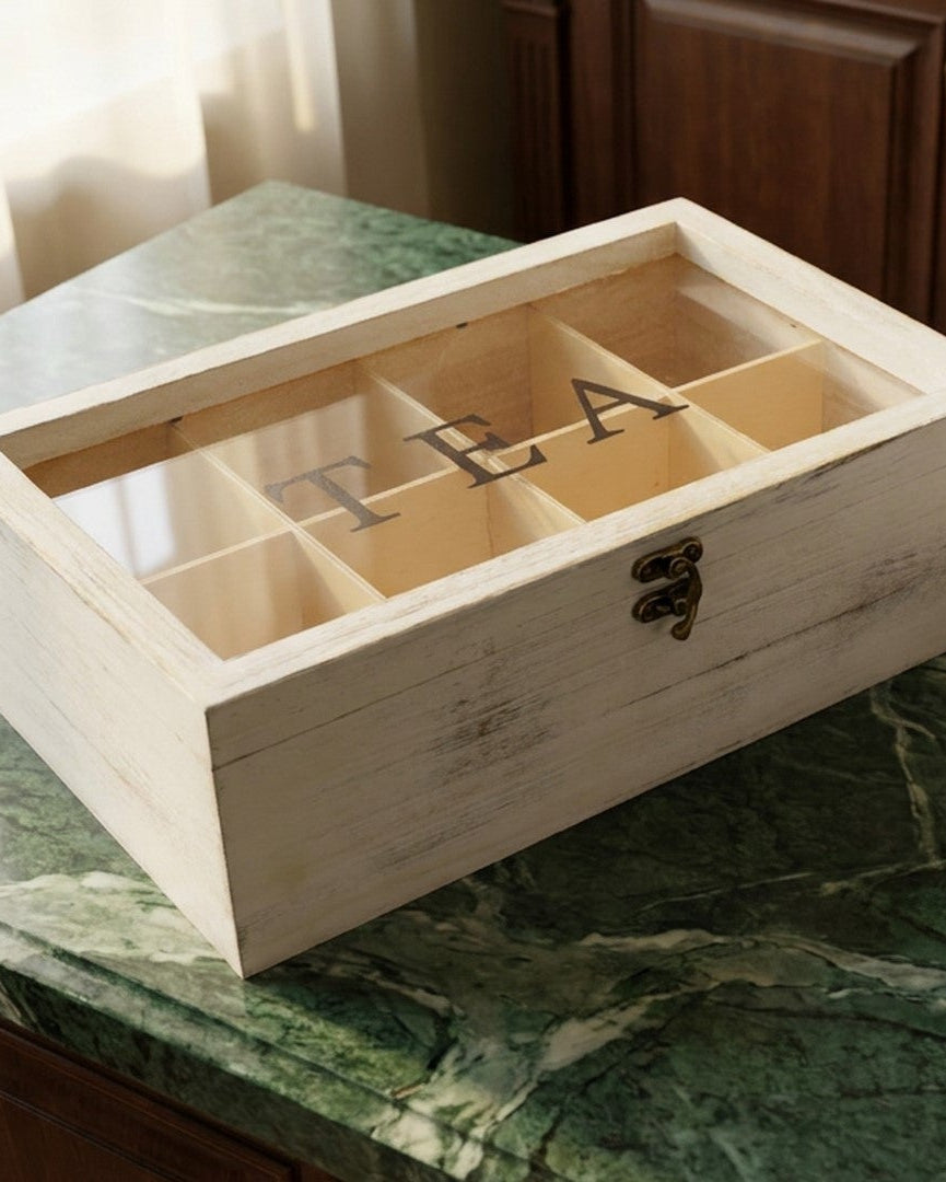 Wooden tea box labeled 'tea' on a kitchen counter with a steaming cup of tea and coffee maker.