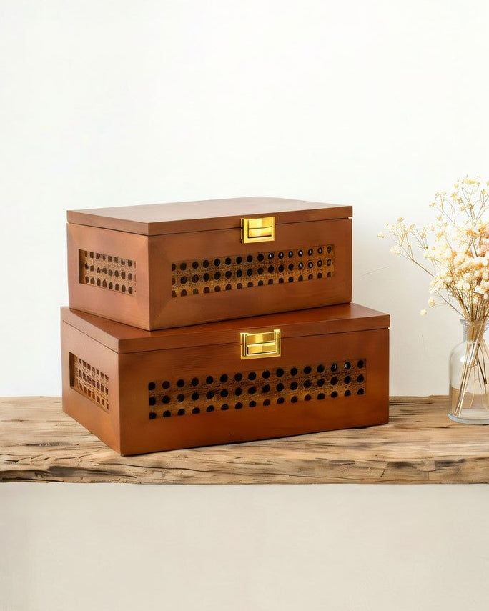 Two wooden storage boxes with lattice designs on a surface with a plant in the background.