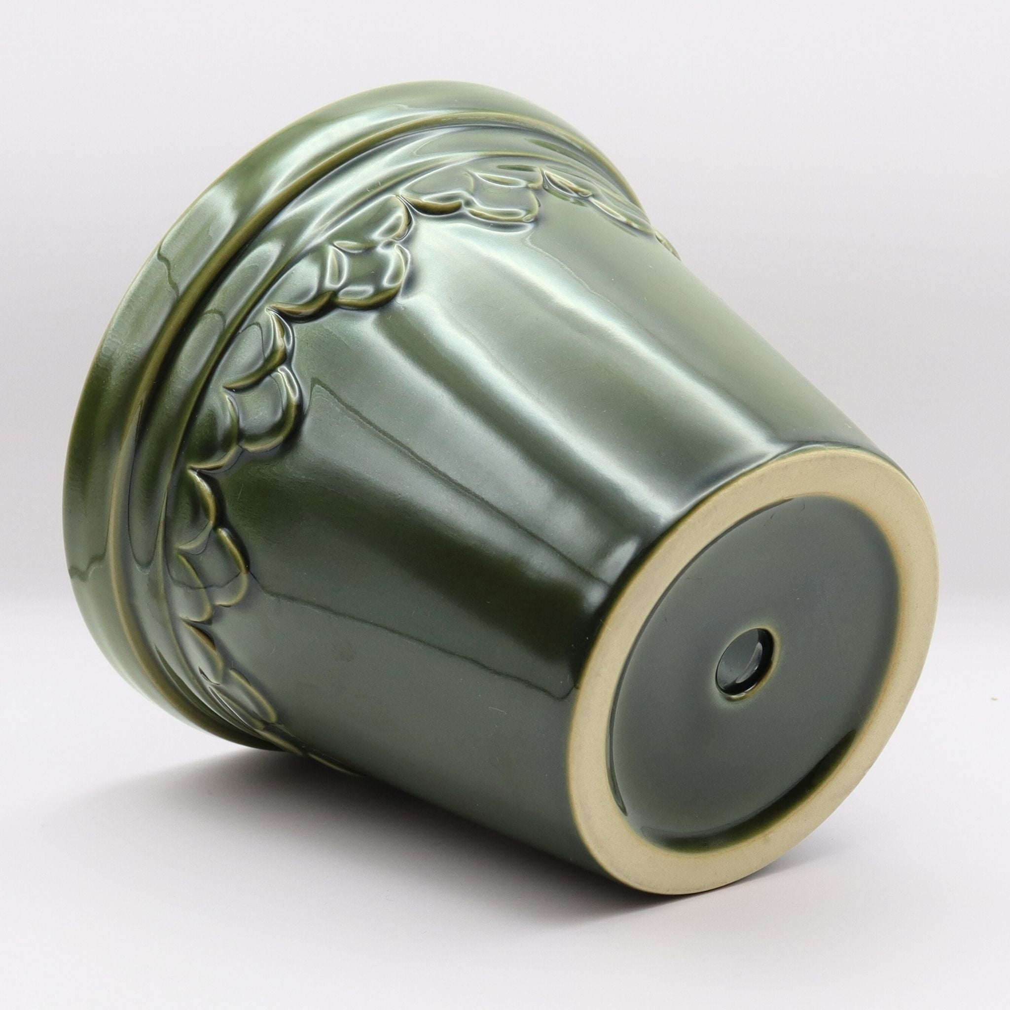 Green ceramic pot with decorative patterns and eucalyptus leaves on a white background