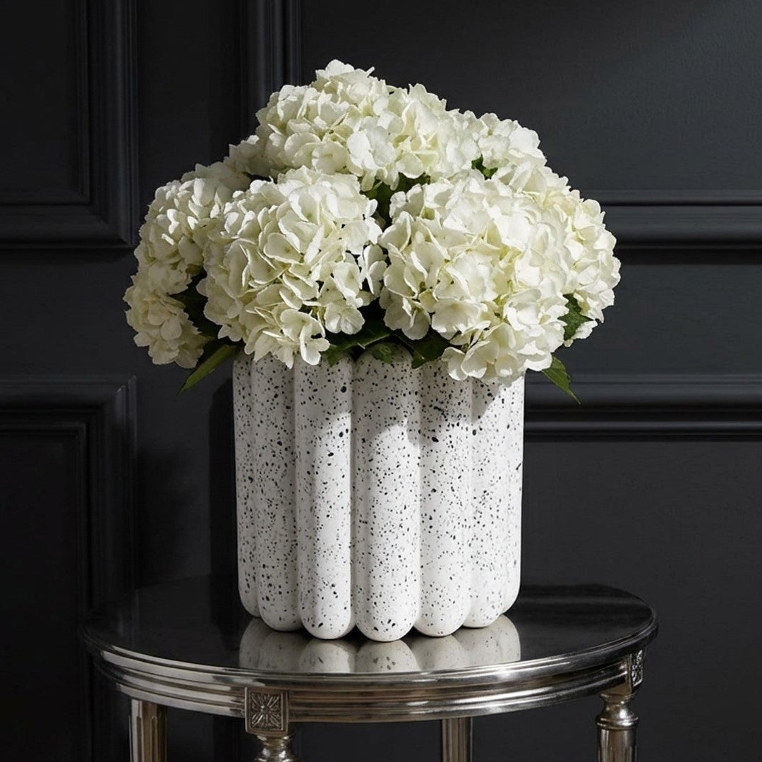 Speckled white vase with black dots next to a green plant