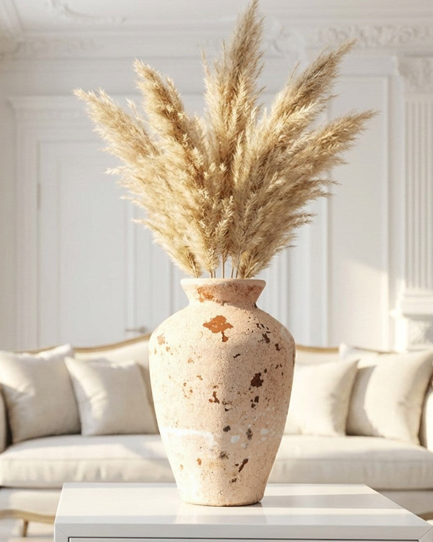 Decorative vase with dried pampas grass on a white surface in a bright room.