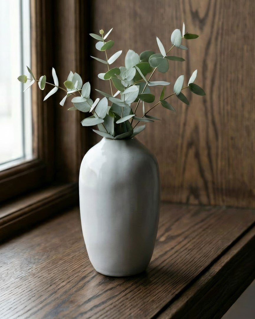 White vase with greenery on a wooden windowsill