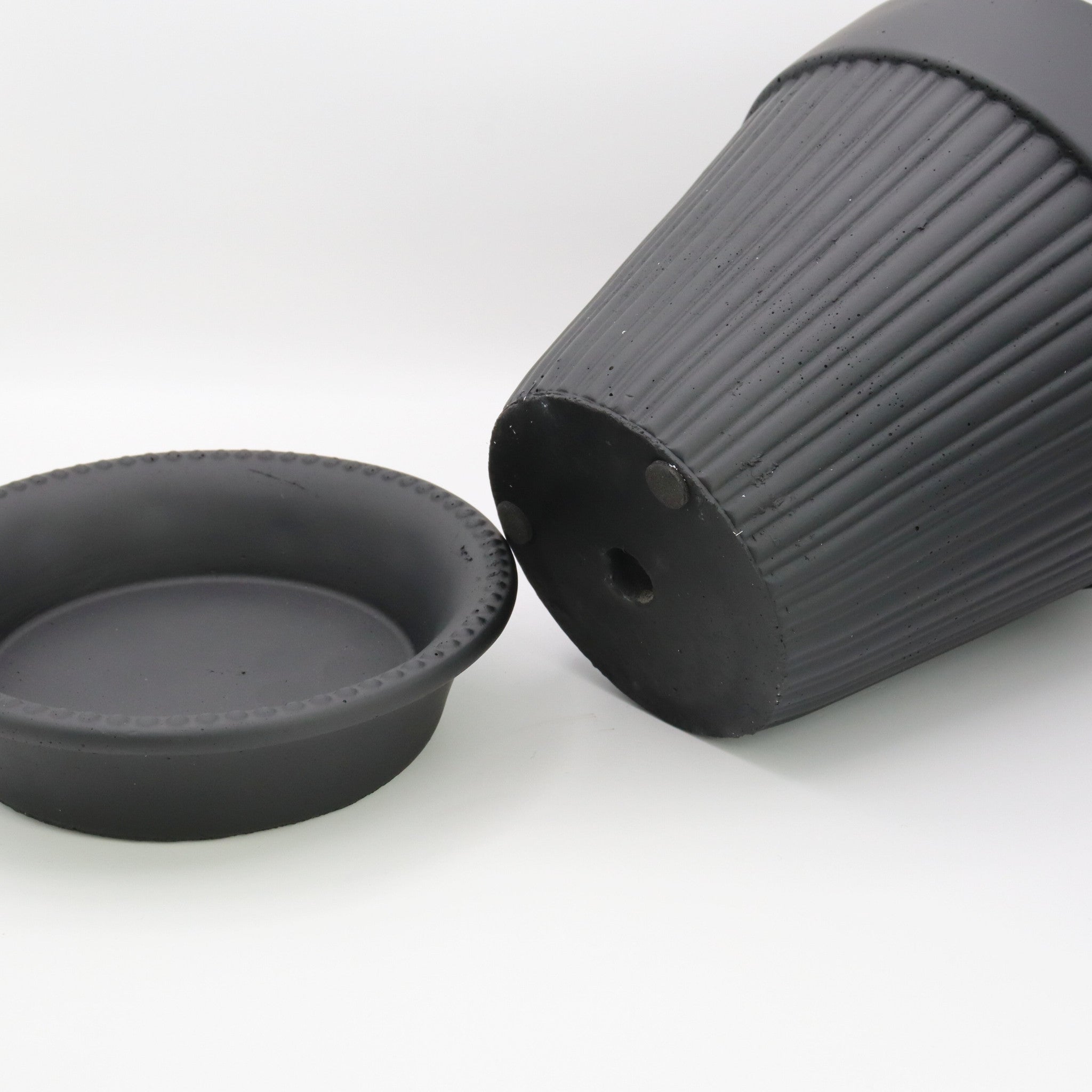 Close-up of a black ribbed pot with matching saucer on a white background