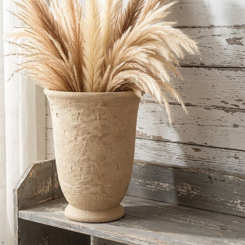 Beige vase with pampas grass on a wooden shelf against a rustic wooden wall.