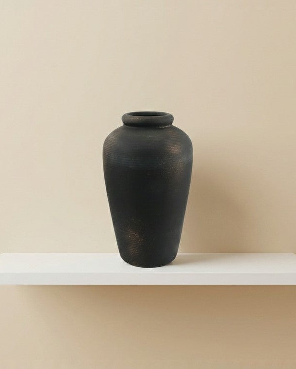 Black vase on a white shelf against a beige wall
