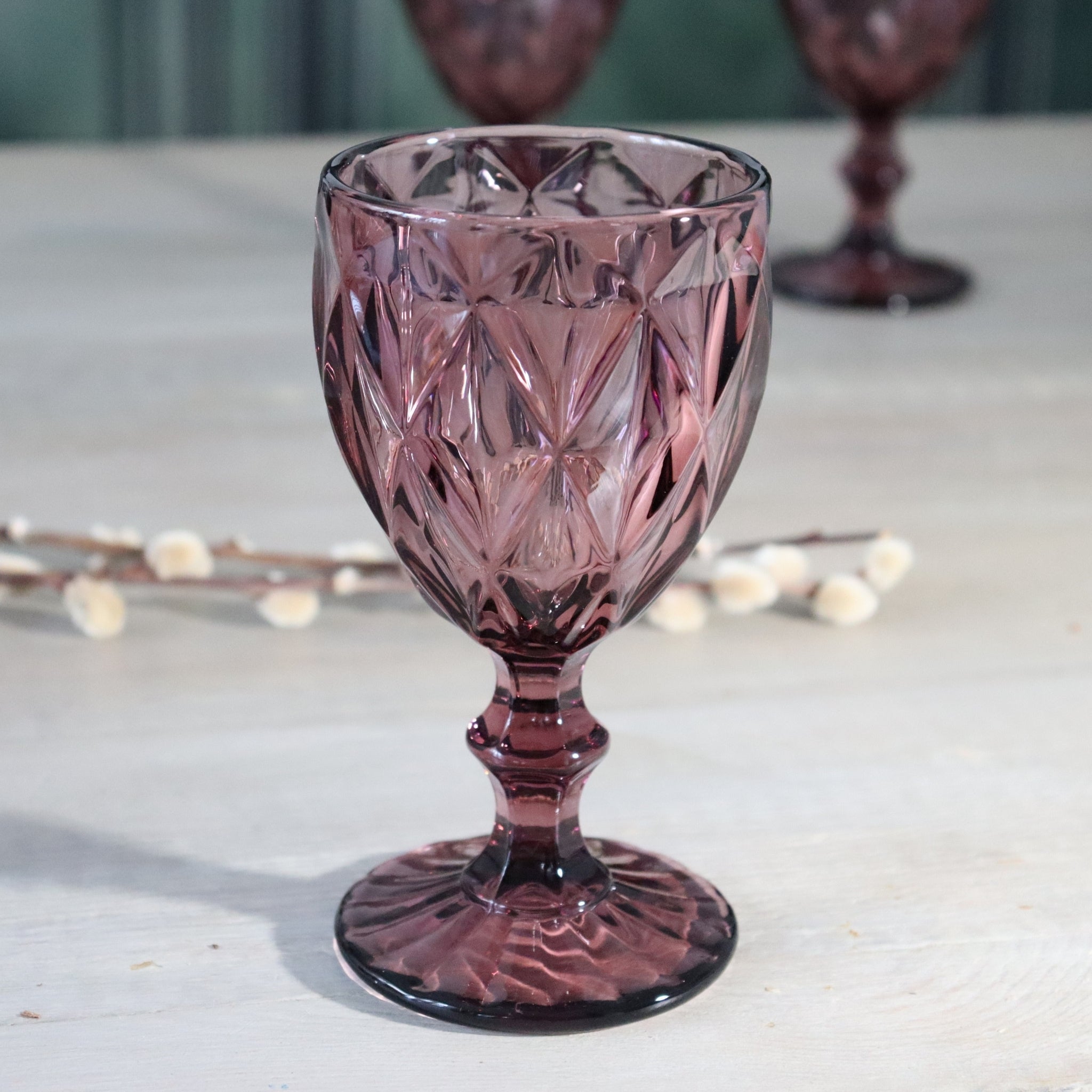 Pink/Purple/Rose glass goblet on a light surface with blurred lights in the background