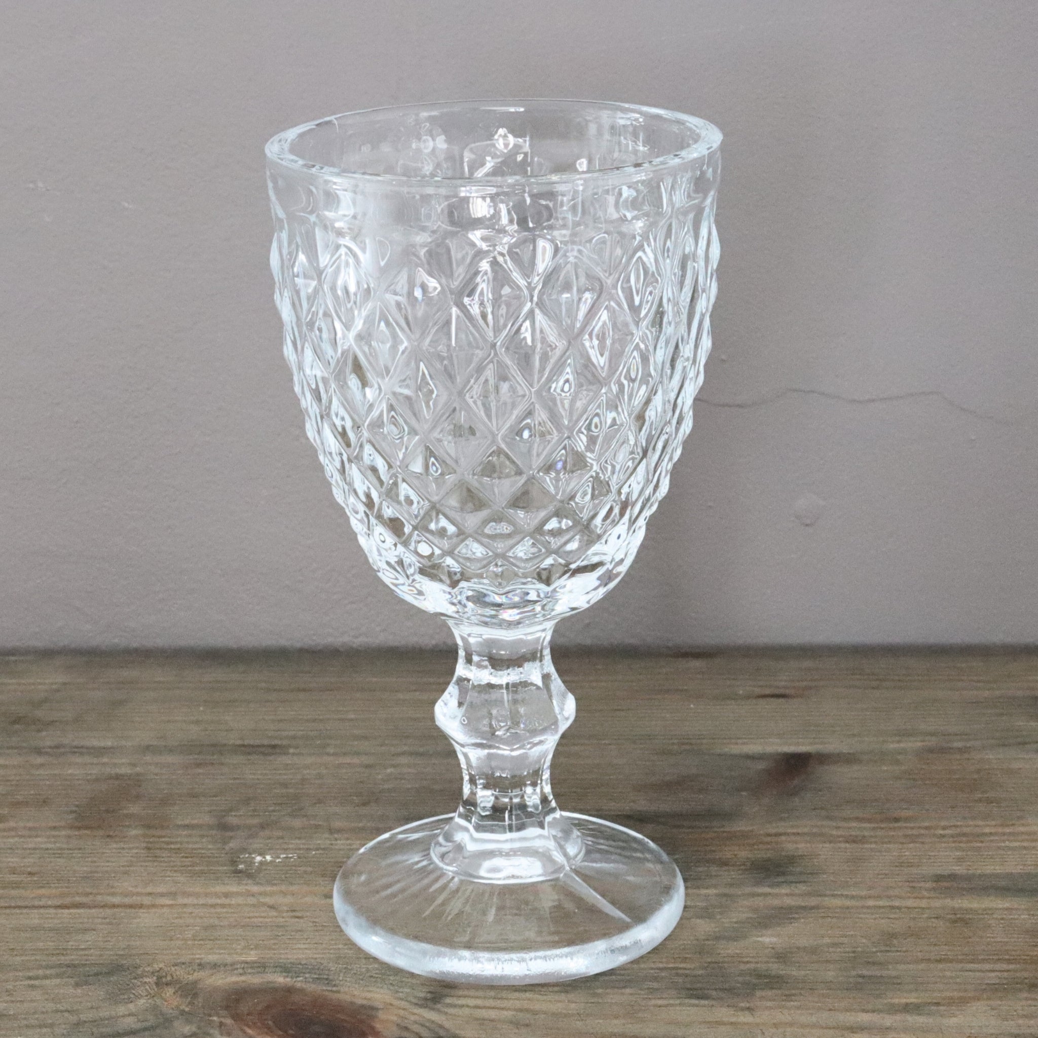Clear glass goblet with diamond pattern on a wooden surface