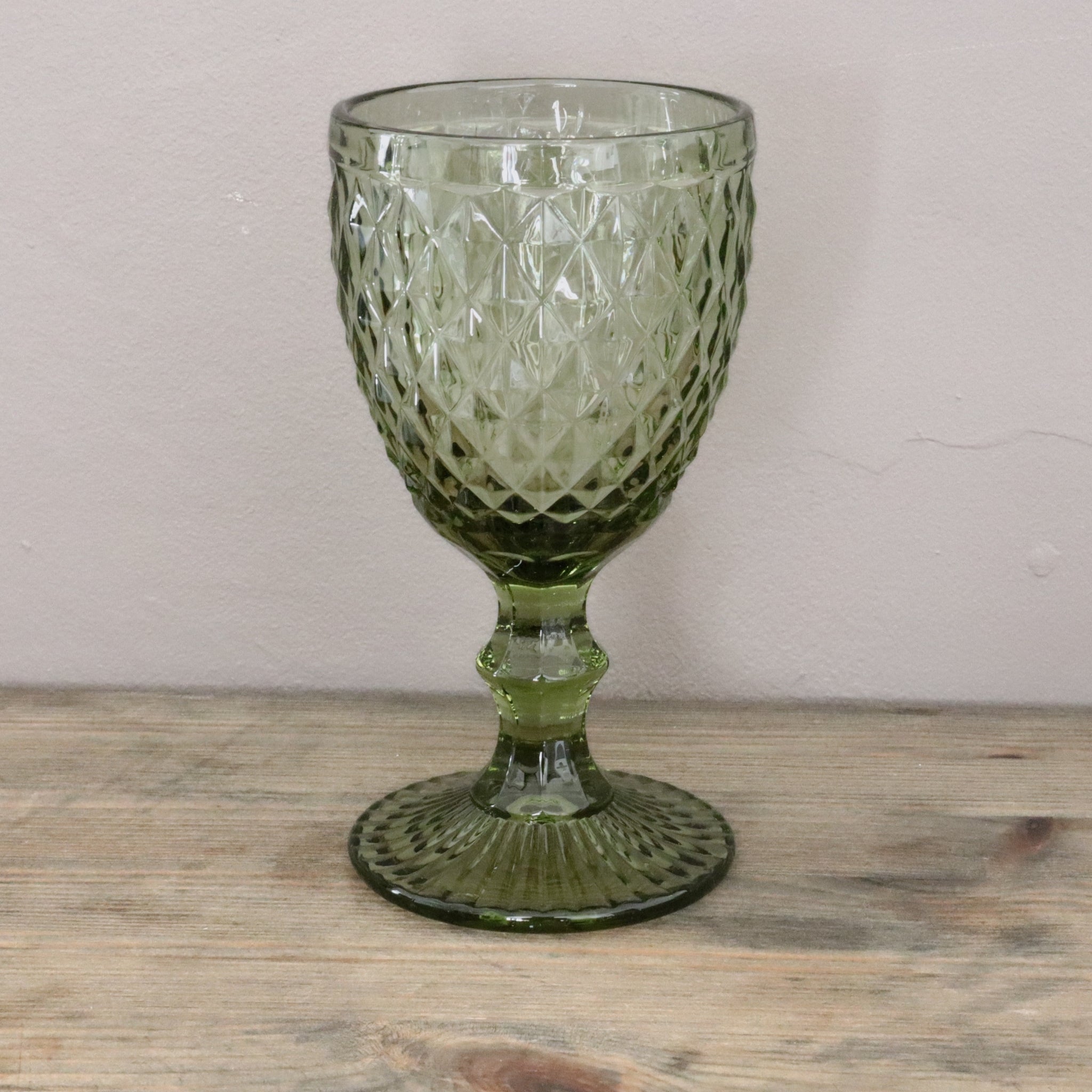 Green glass goblet with textured design on a wooden surface and light gray background