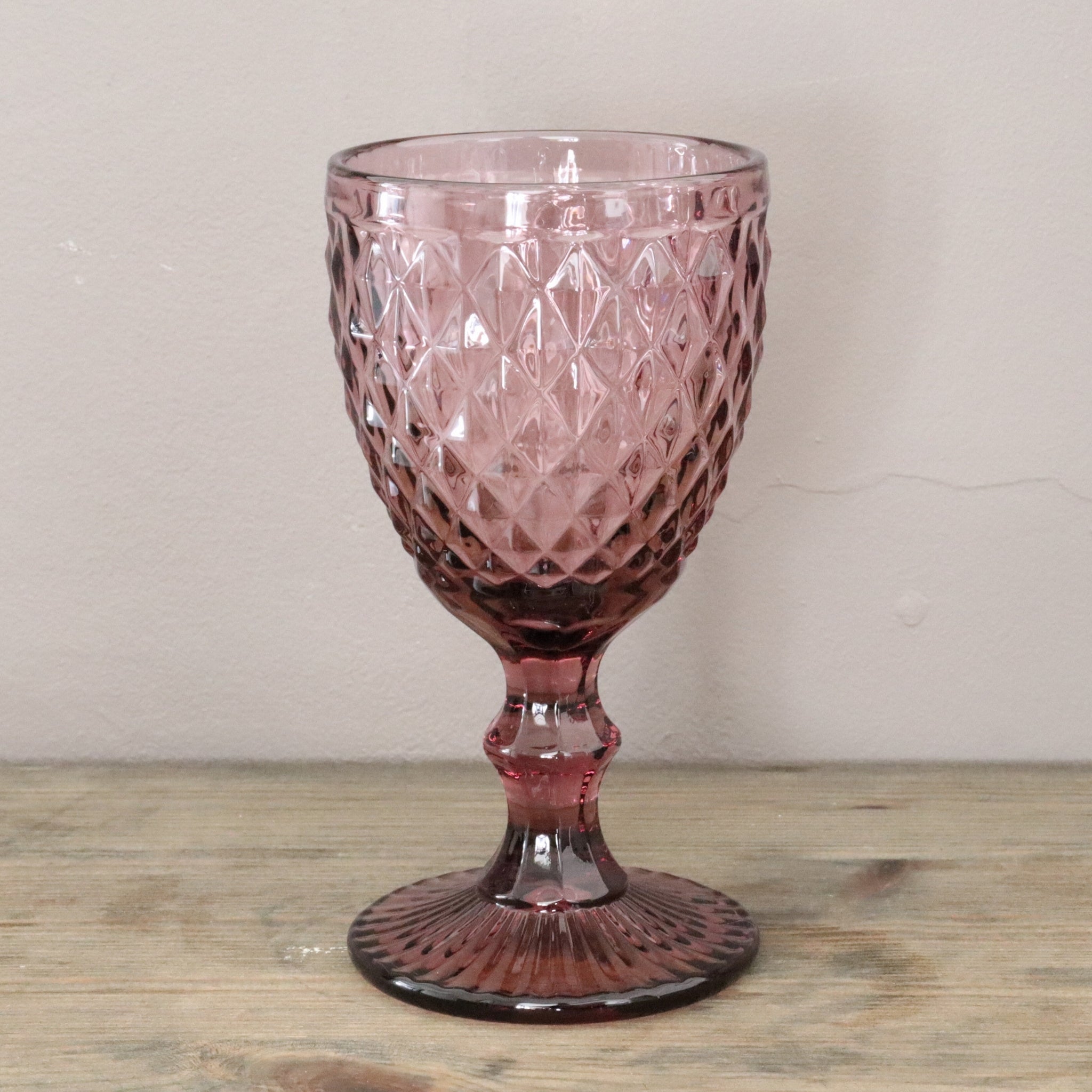 Pink glass goblet with diamond pattern on a wooden surface