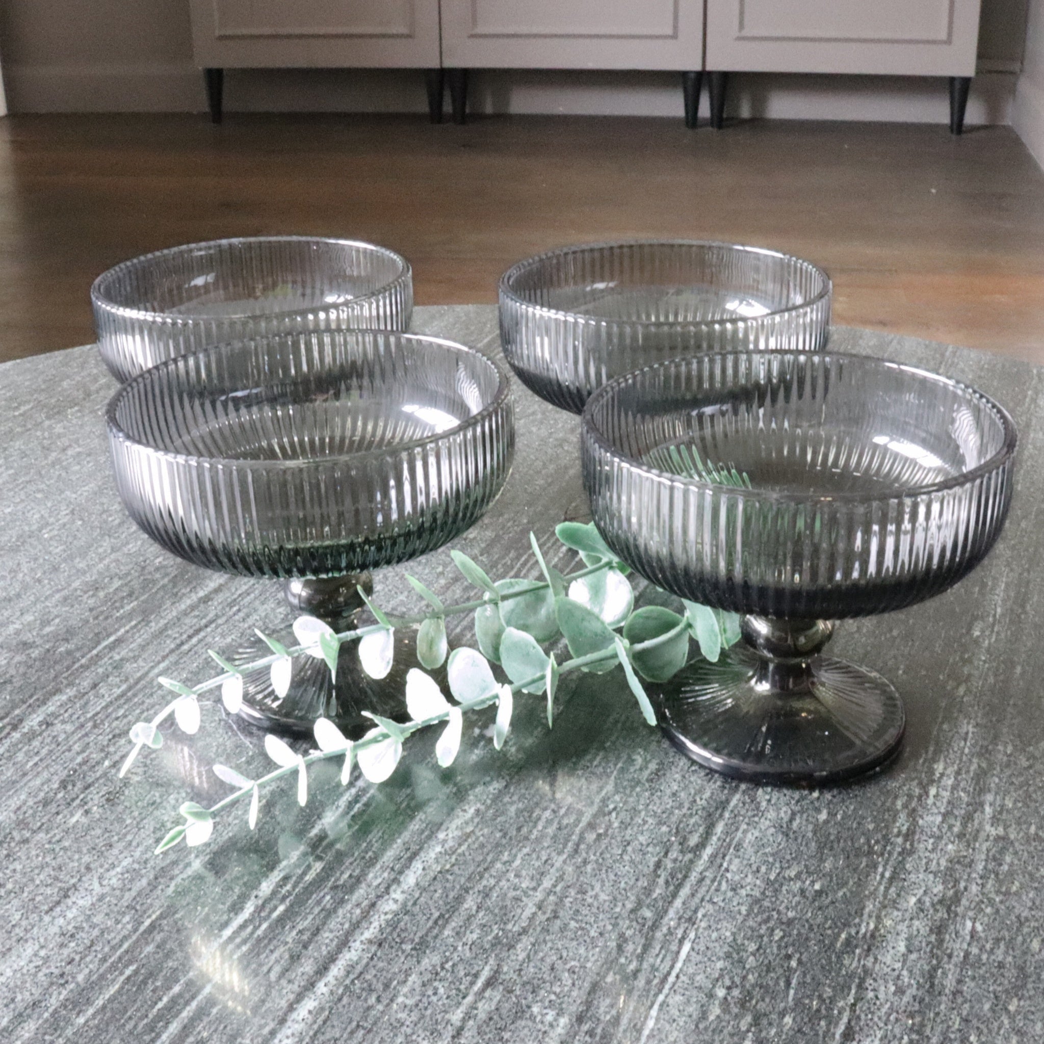 Four ribbed glass bowls on a textured surface with a branch of eucalyptus.
