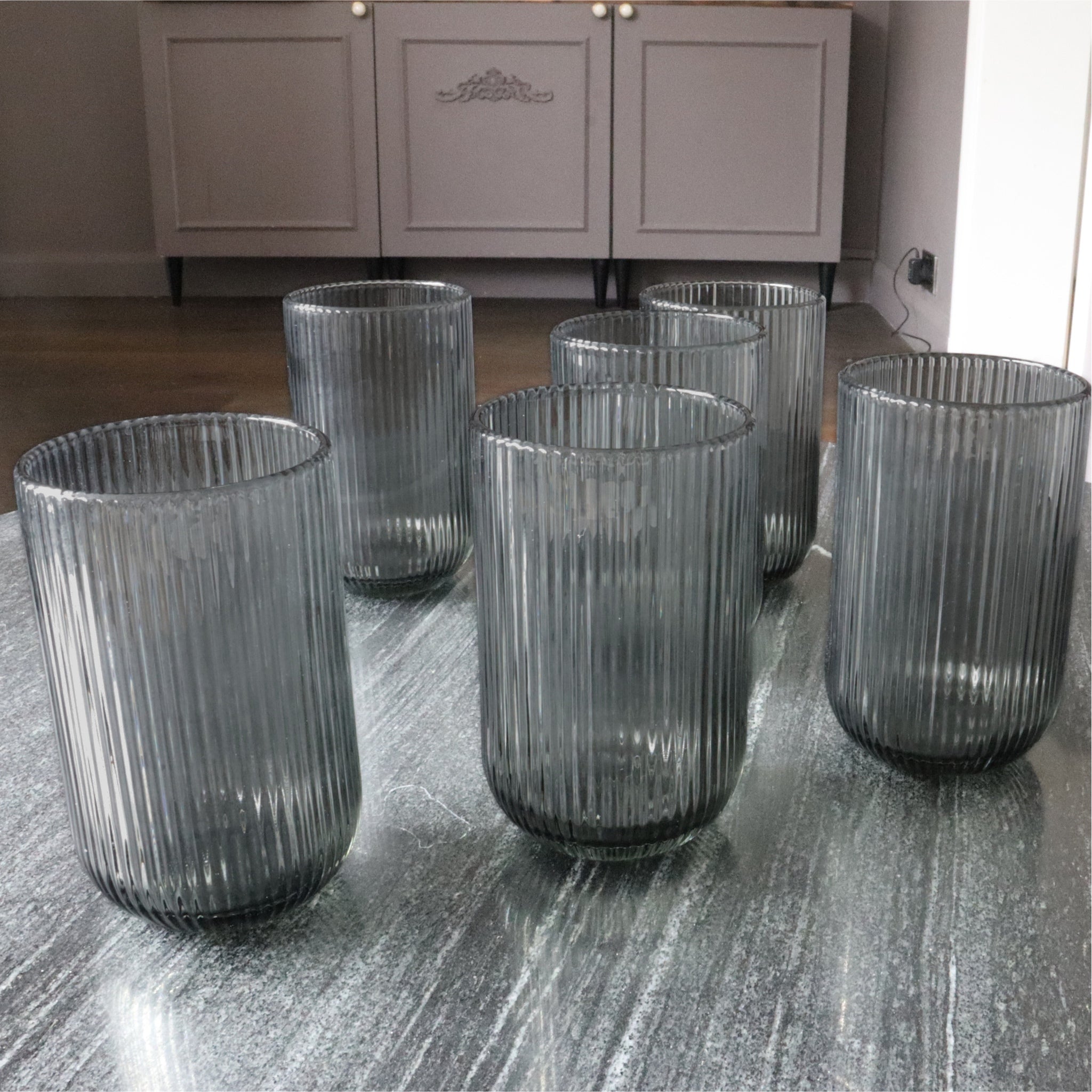 Set of six ribbed glass tumblers on a wooden surface with a neutral background