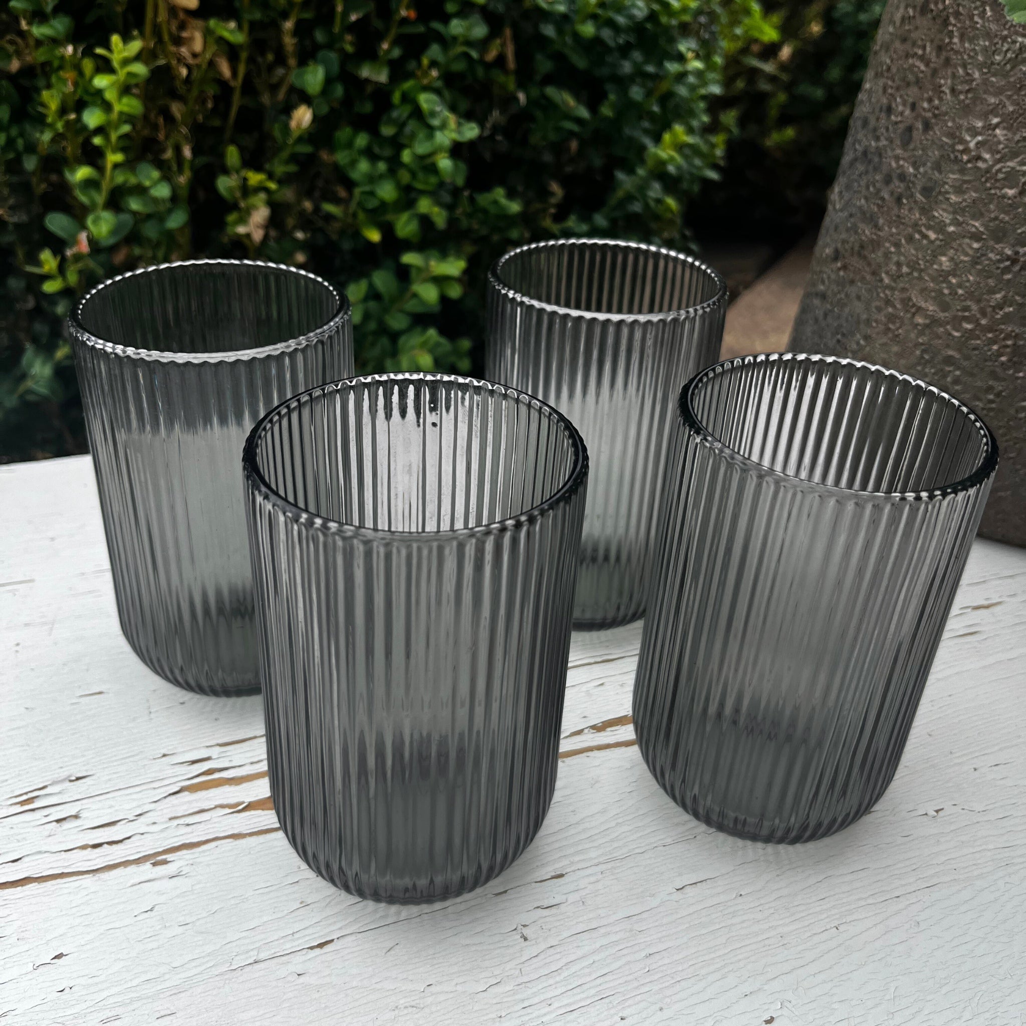 Four ribbed glass tumblers on a wooden surface with a natural background