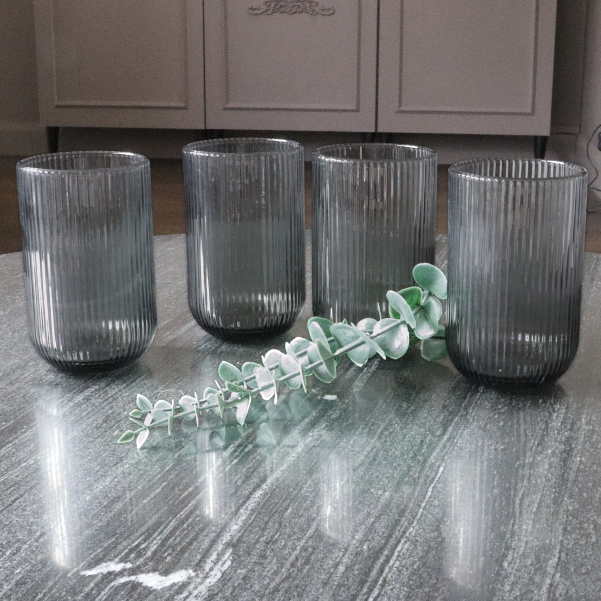 Set of four ribbed glass tumblers on a reflective surface with a blurred background
