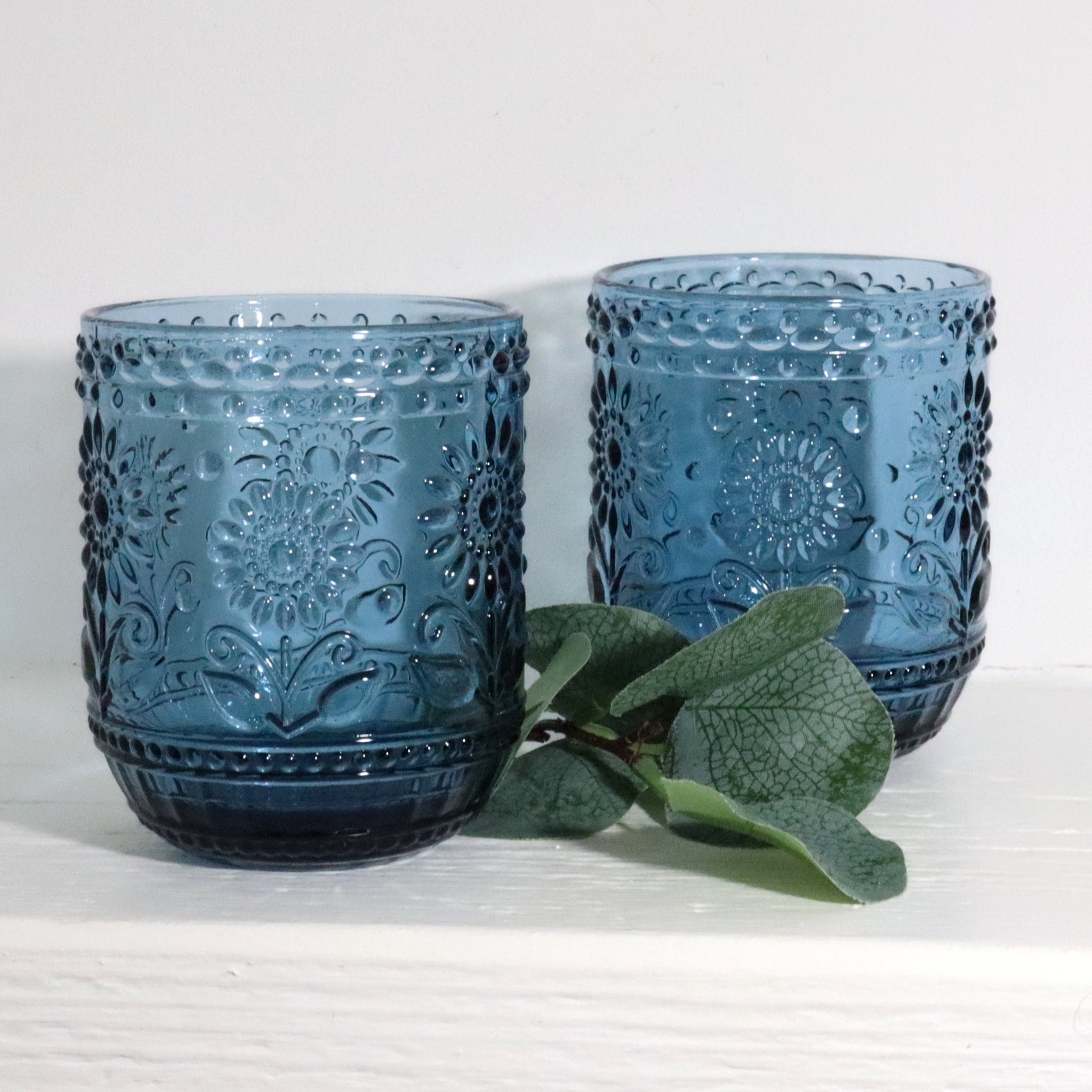 Two blue glass tumblers with embossed designs on a white surface.