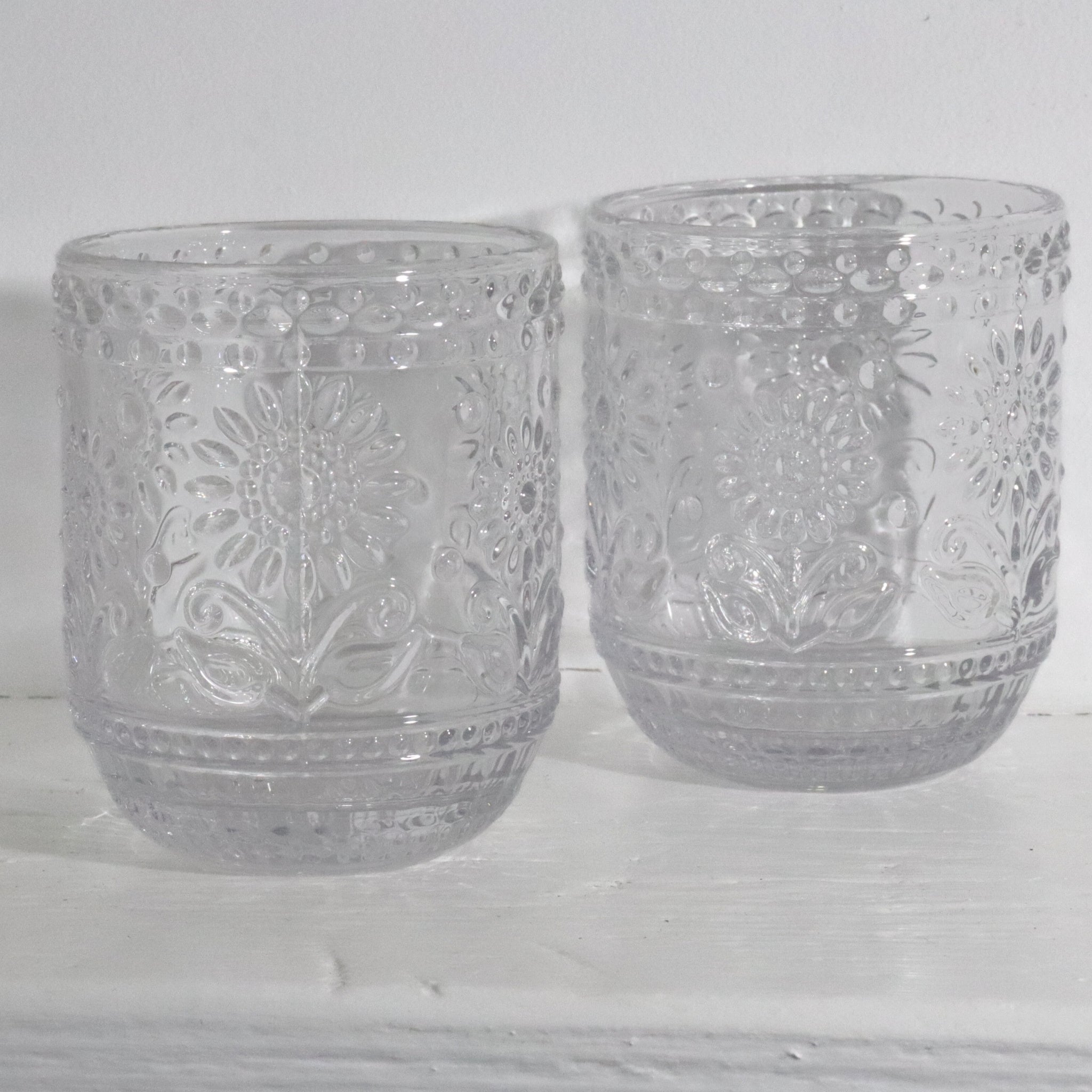 Two clear glass tumblers with floral patterns on a white wooden surface