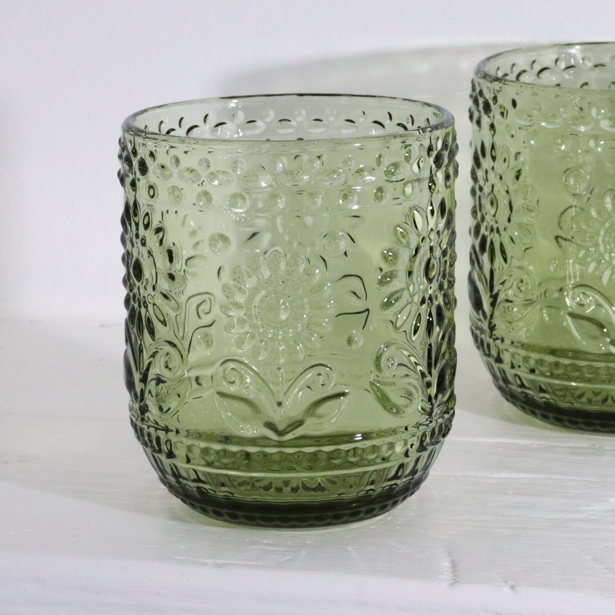 Two green glass tumblers with embossed designs on a white background