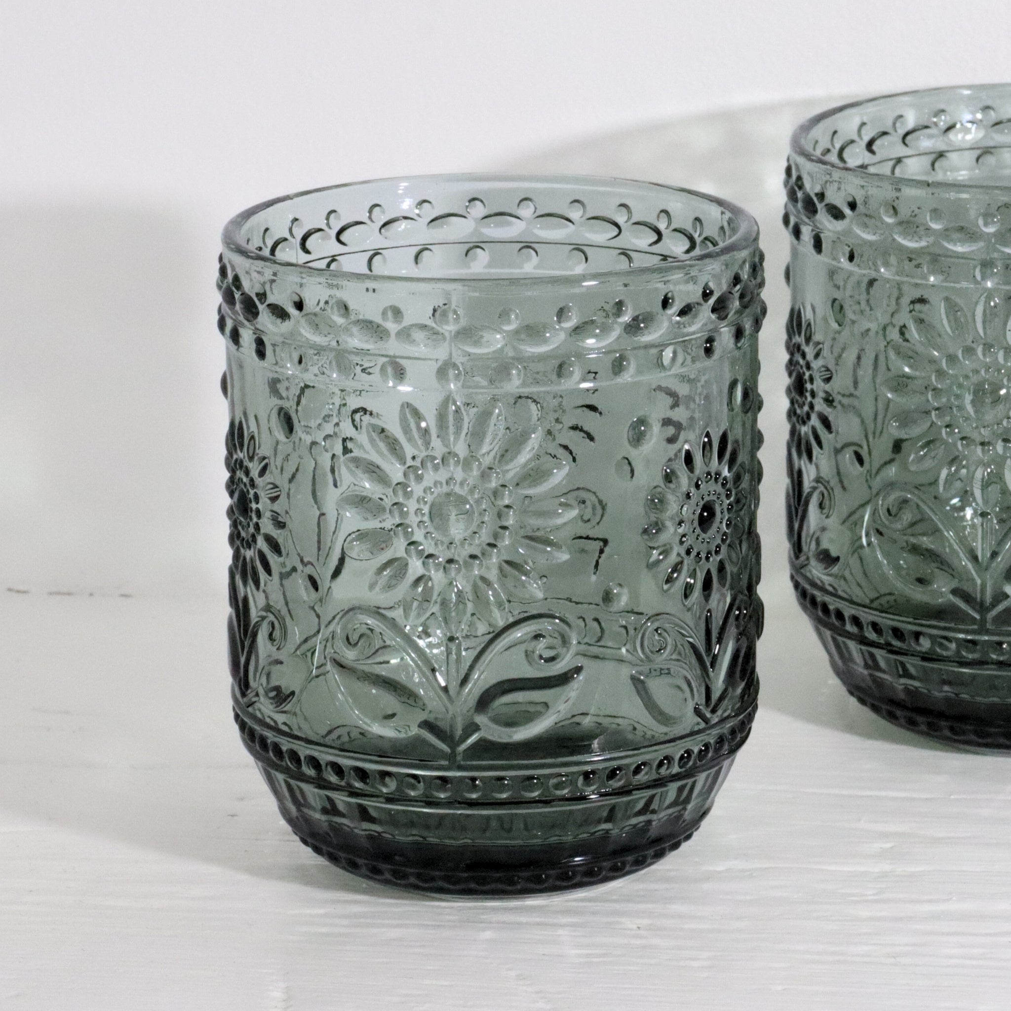 Two gray glass tumblers with floral patterns on a white surface