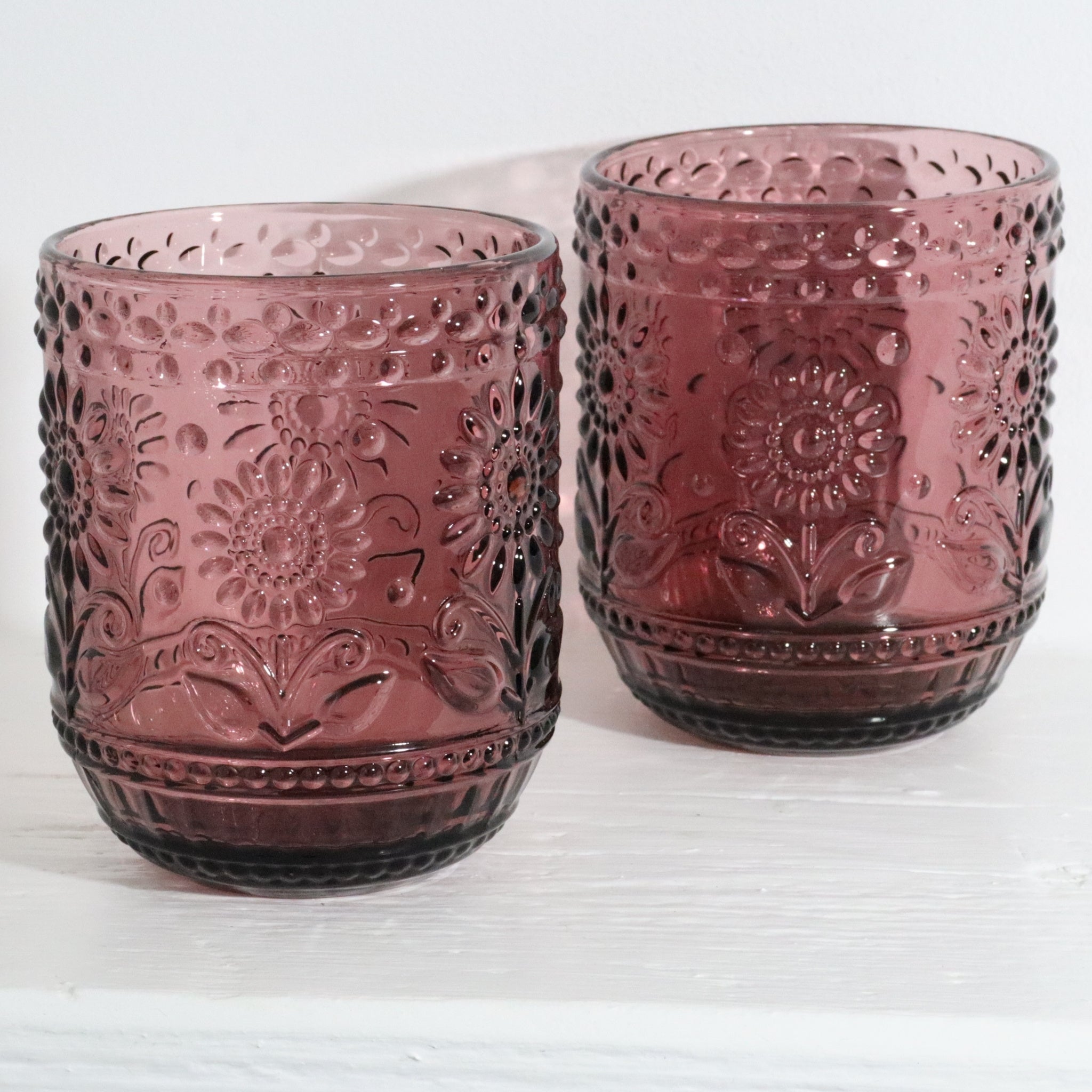 Two pink glass tumblers with embossed designs on a white background