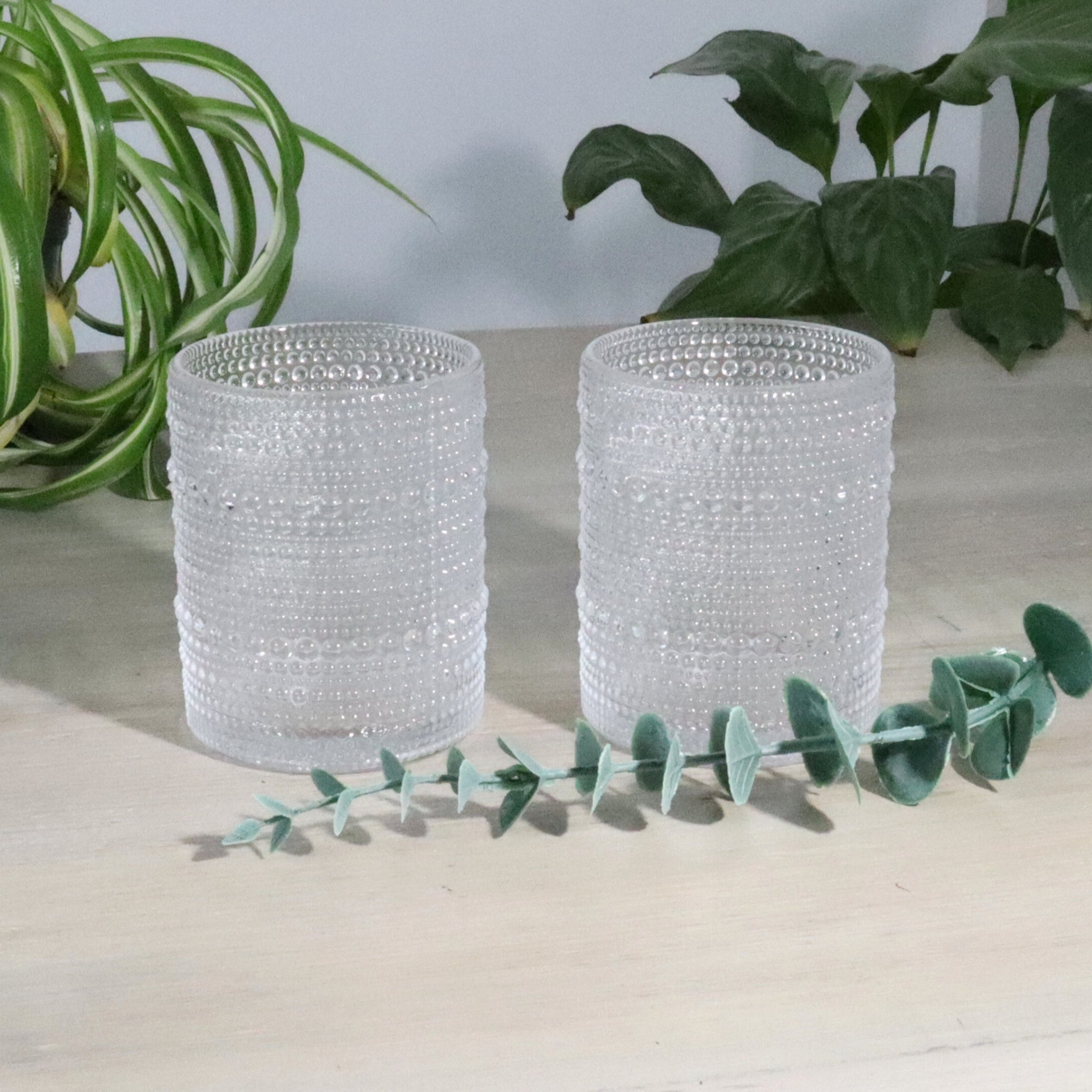 Two hobnail glass tumblers on a light surface with greenery in the background