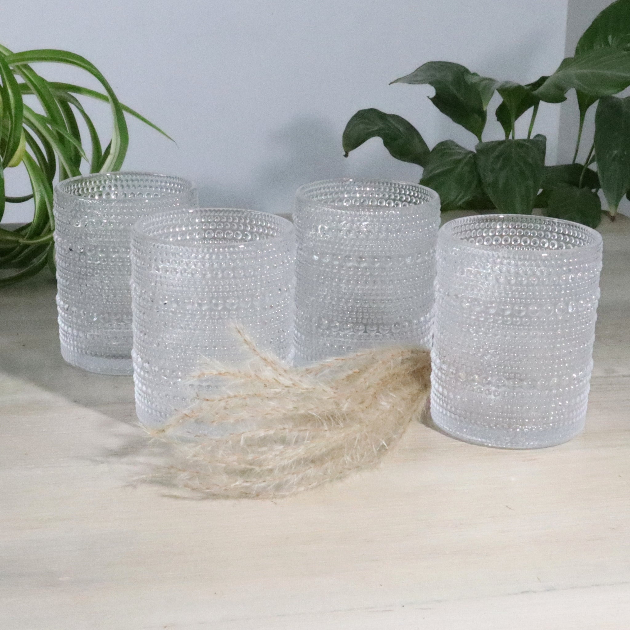 Set of four hobnail glass rock tumblers on a light surface with plants in the background