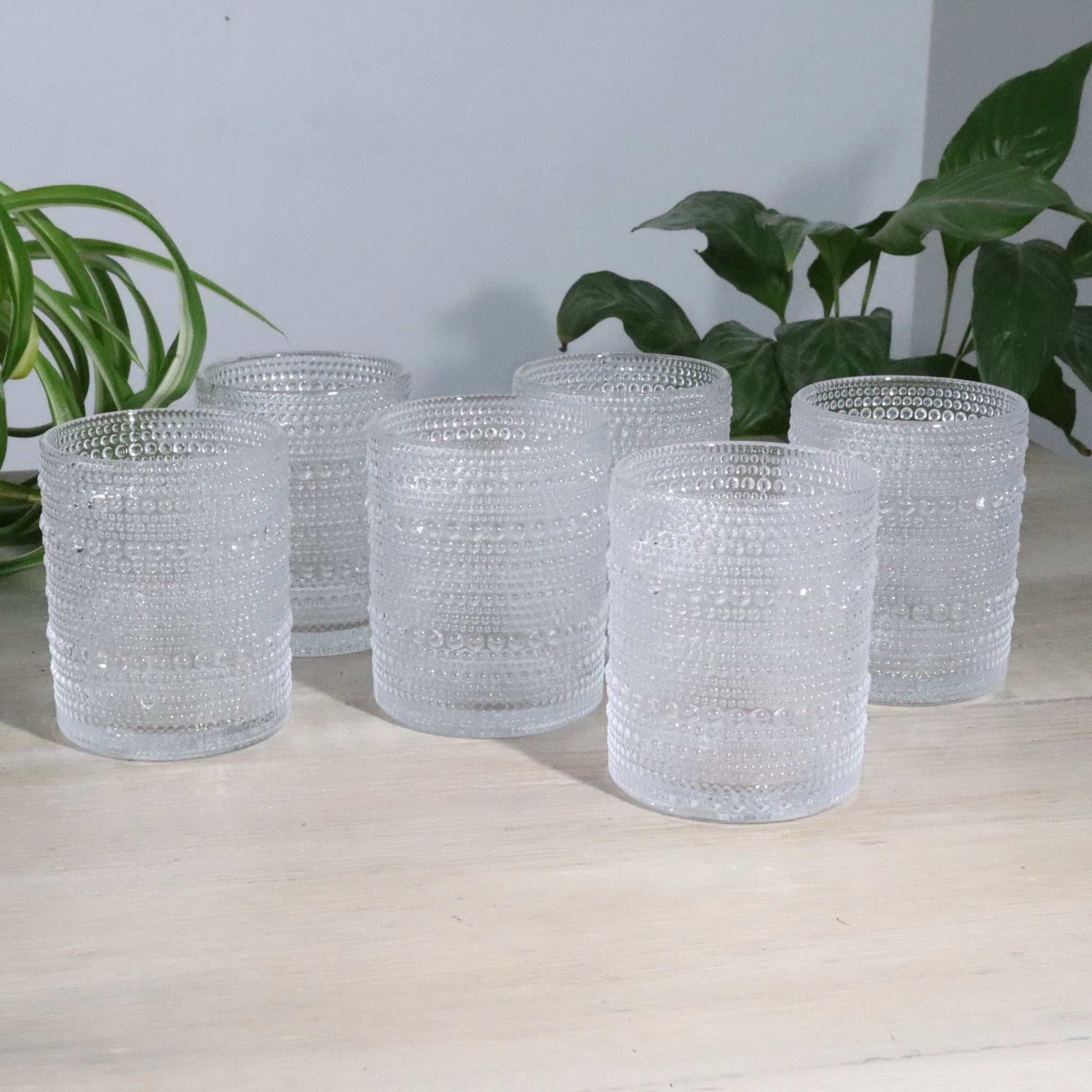 Set of hobnail glass tumblers on a light surface with plants in the background