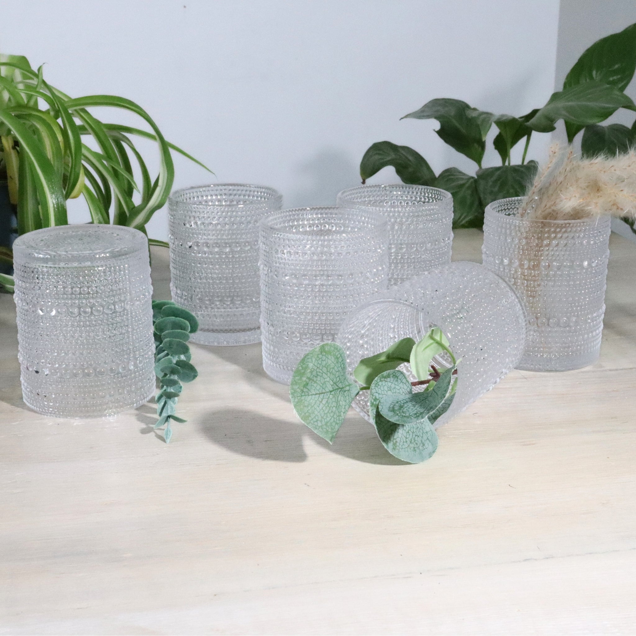 Set of hobnail glass tumblers on a light surface with plants in the background