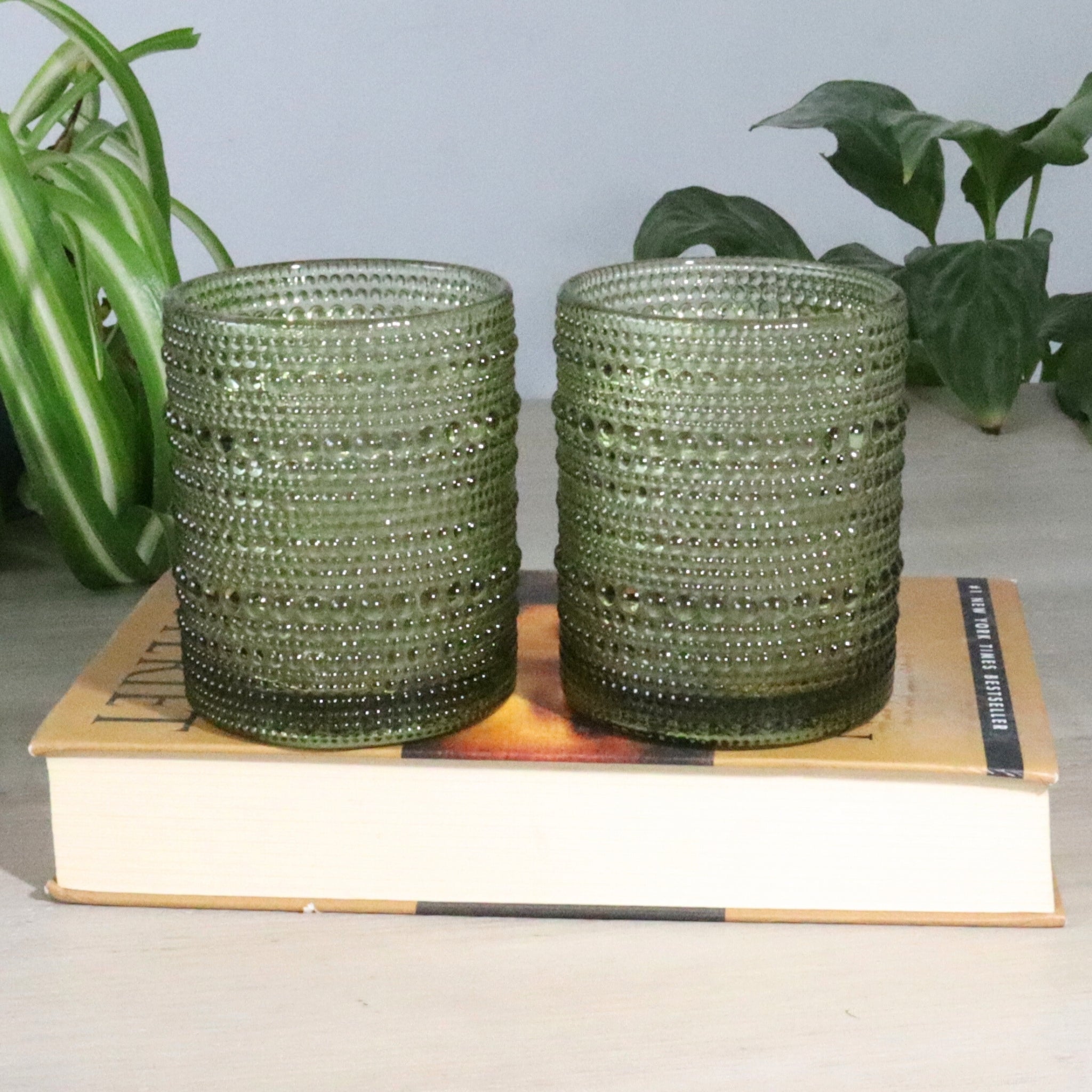 Two green beaded hobnail glass tumblers on a book with plants