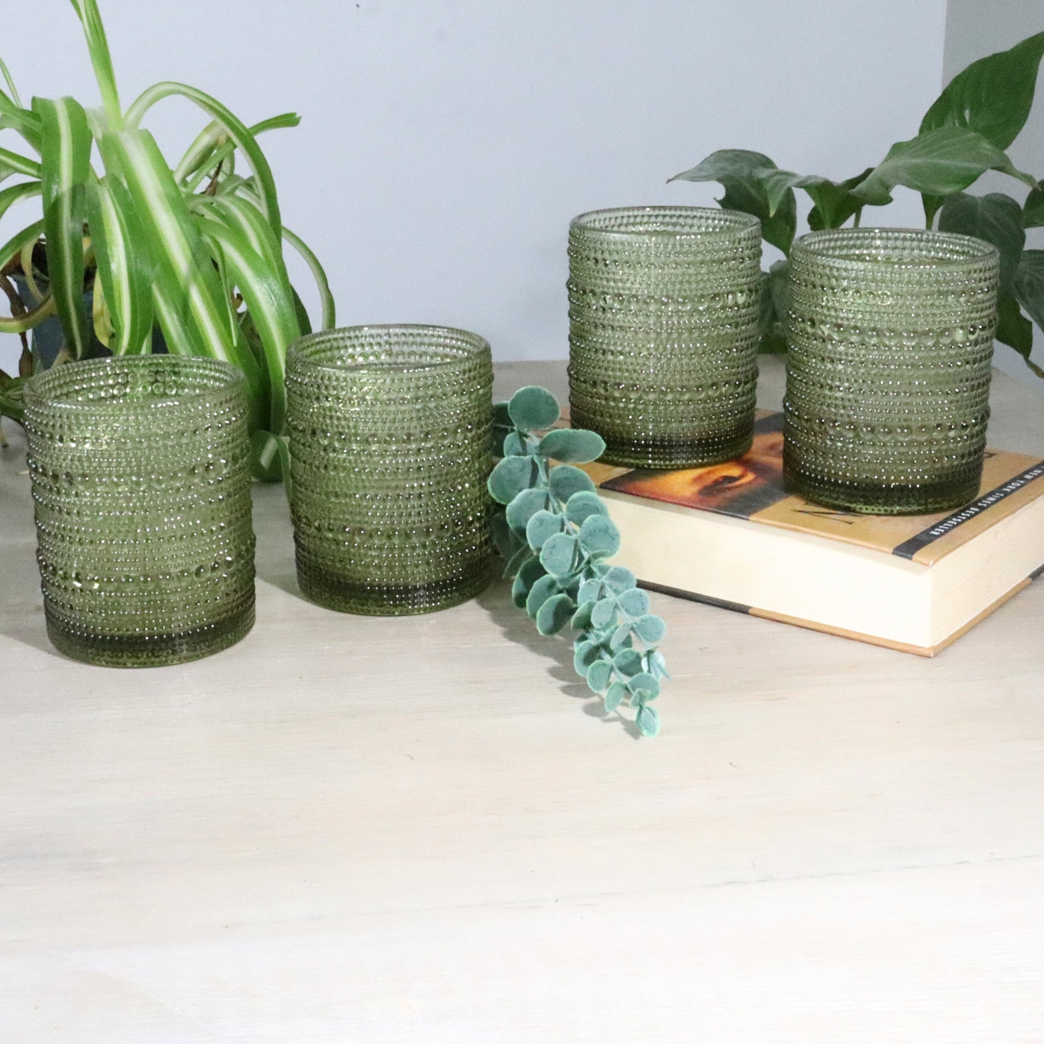 Set of green hobnail old fashioned glass tumblers on a surface with plants in the background