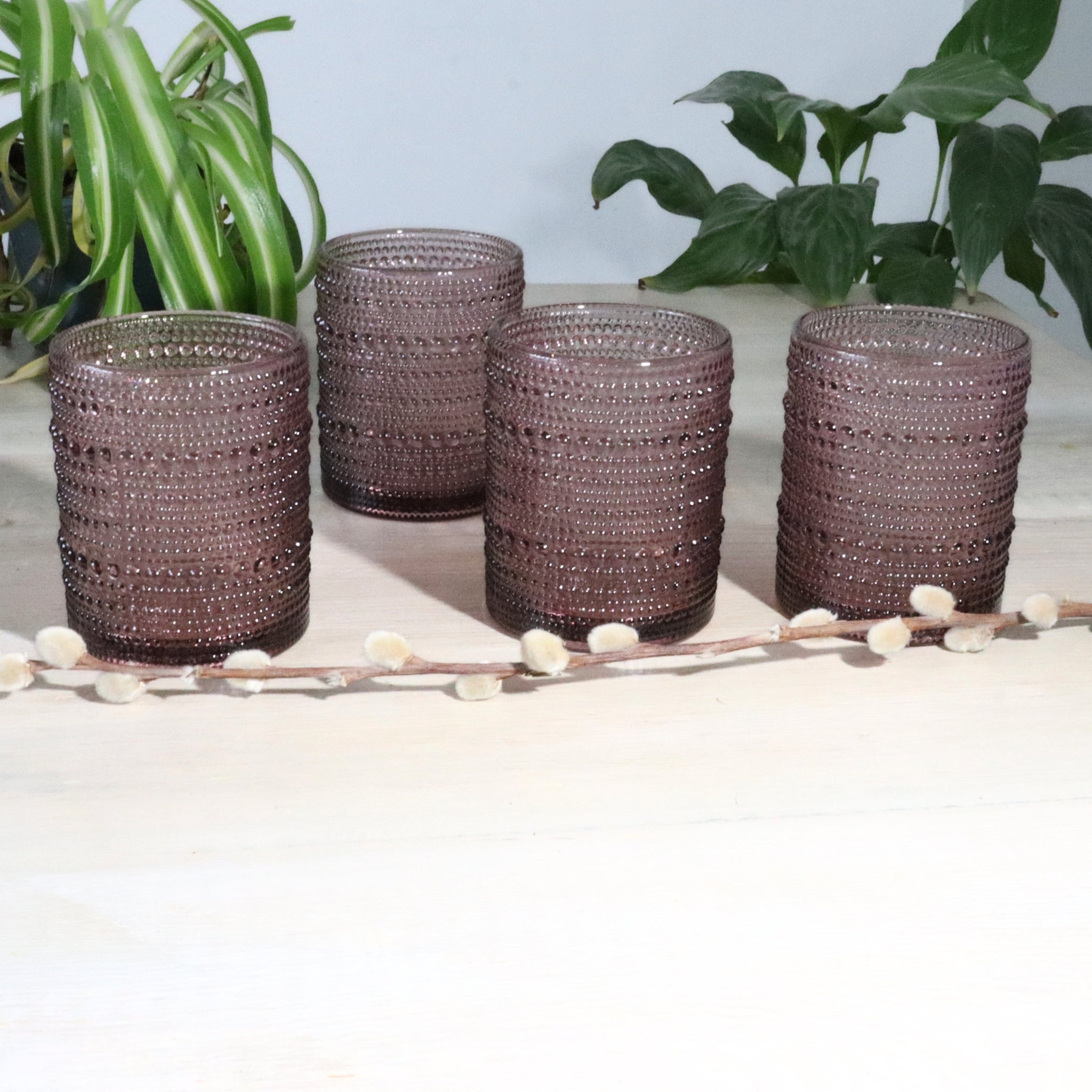 Set of four hobnail glass tumblers on a light surface with plants in the background