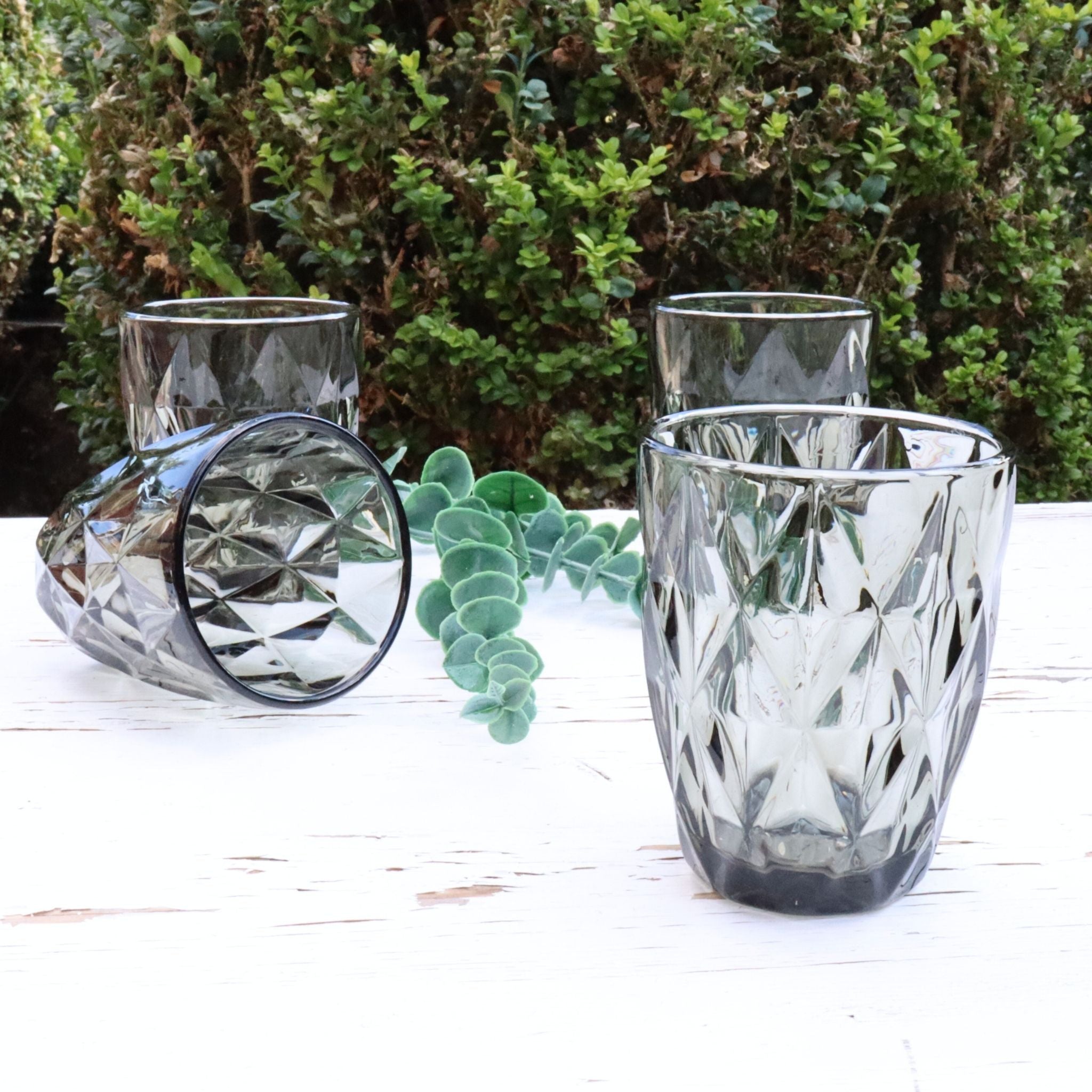 Set of grey glass tumblers with diamond pattern on a white surface with greenery in the background