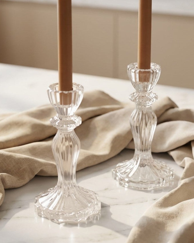 Two clear glass candle holders on a wooden surface with a textured white background.
