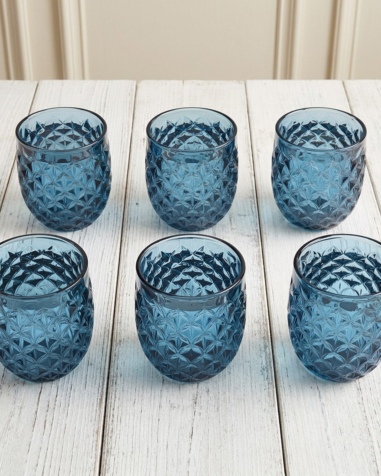 Set of six blue textured glass tumblers on a light surface with greenery.