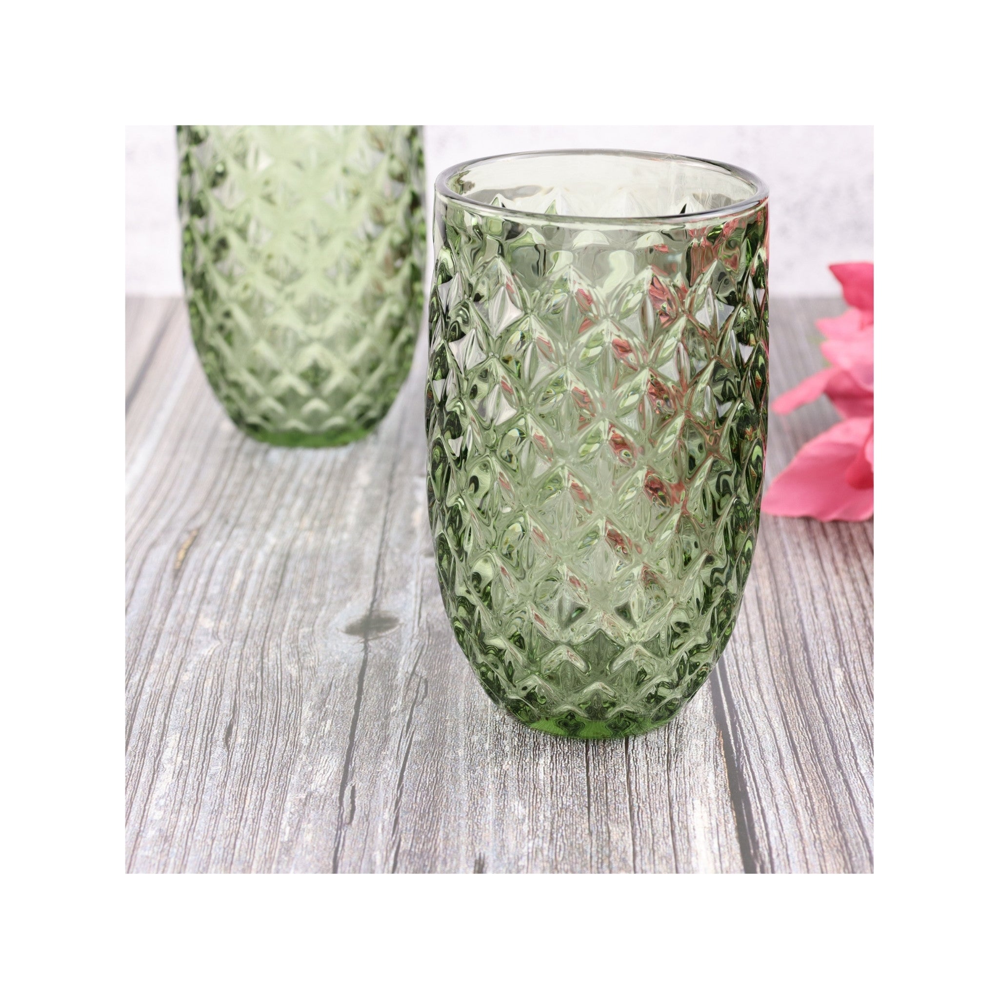Green textured glass tumblers on a wooden surface with pink flowers.