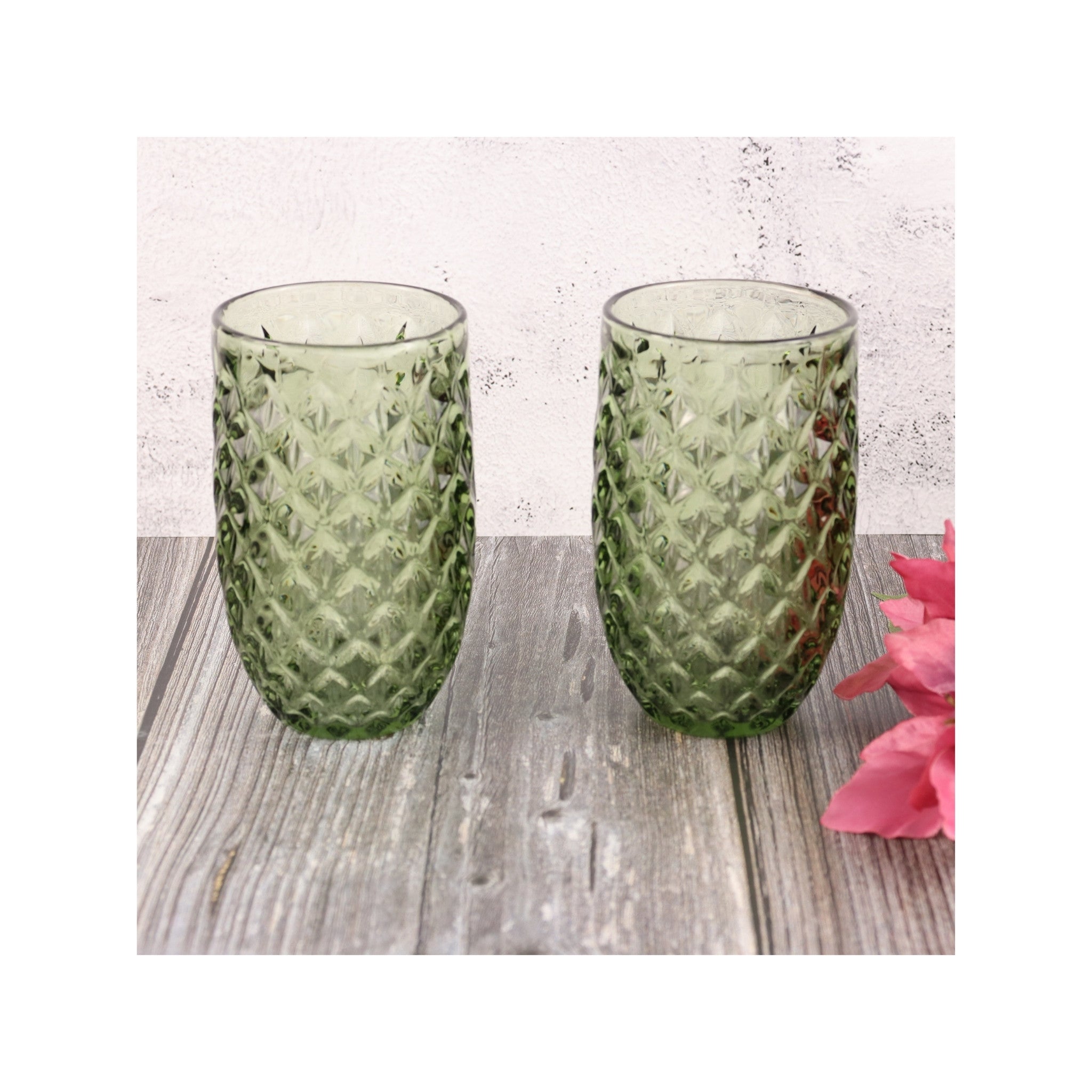 Two green textured glass tumblers on a wooden surface with a pink flower.