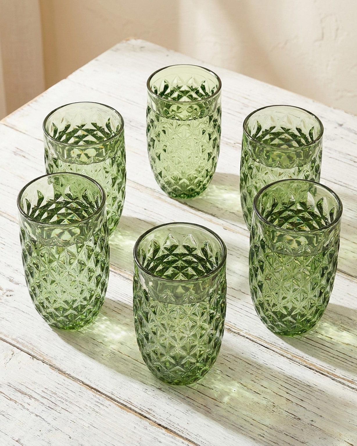 Set of green textured glass tumblers on a wooden surface with a book in the background.