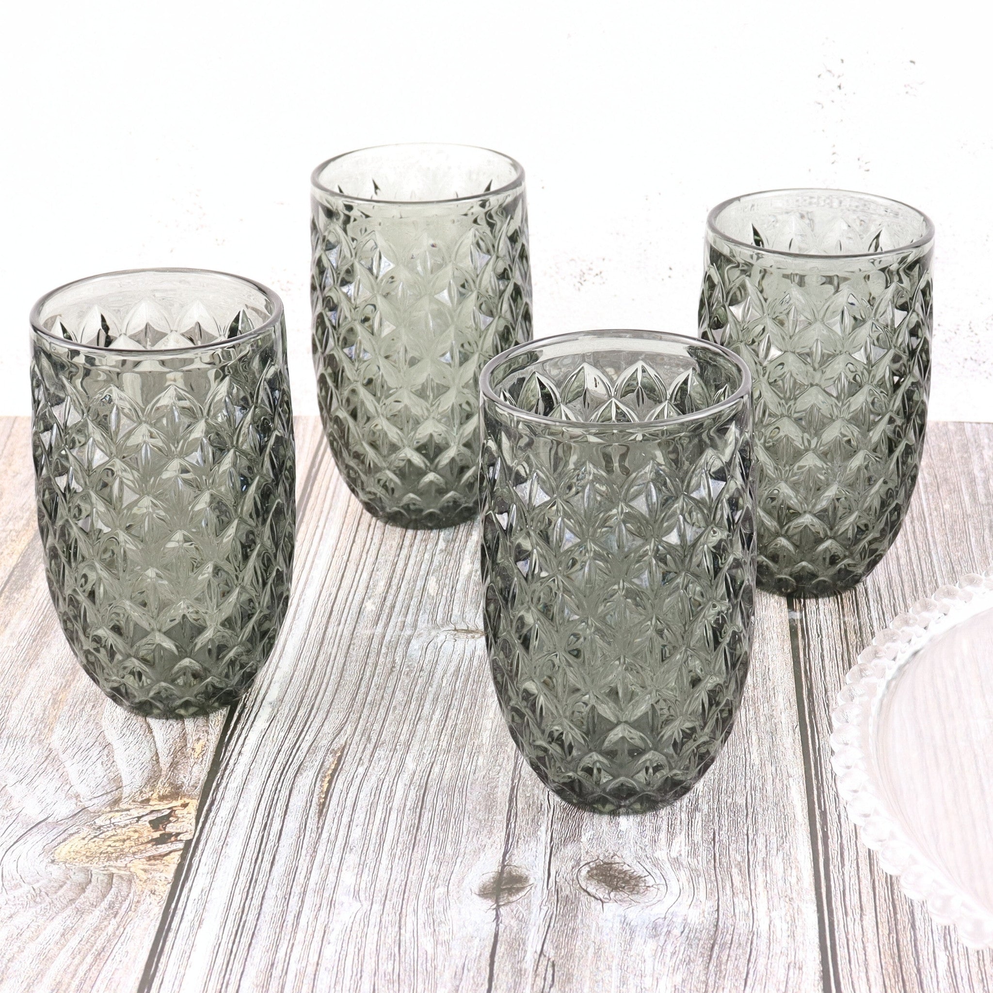 Four green glass tumblers with textured design on a wooden surface
