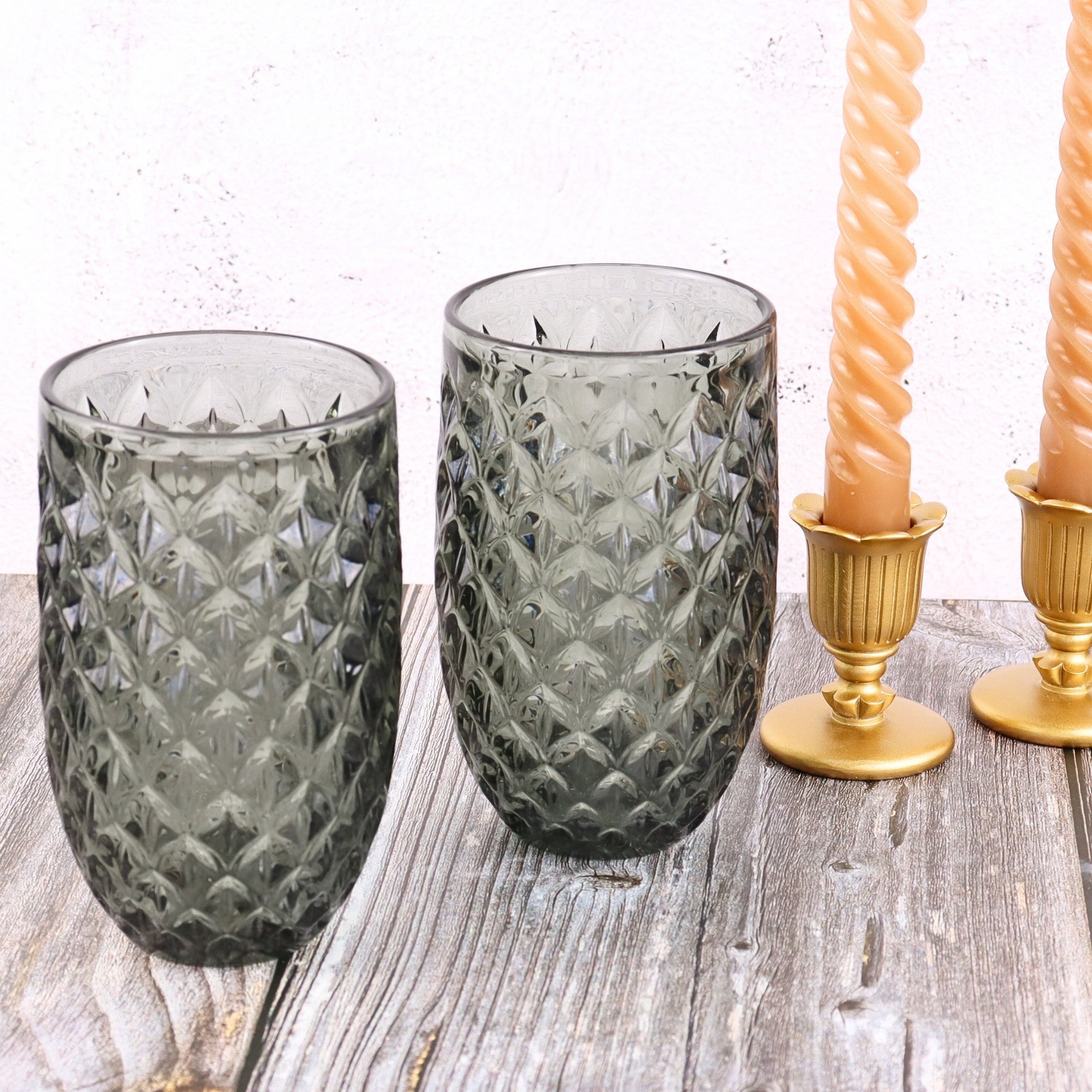 Two textured glass tumblers on a wooden surface with gold candle holders and candles.