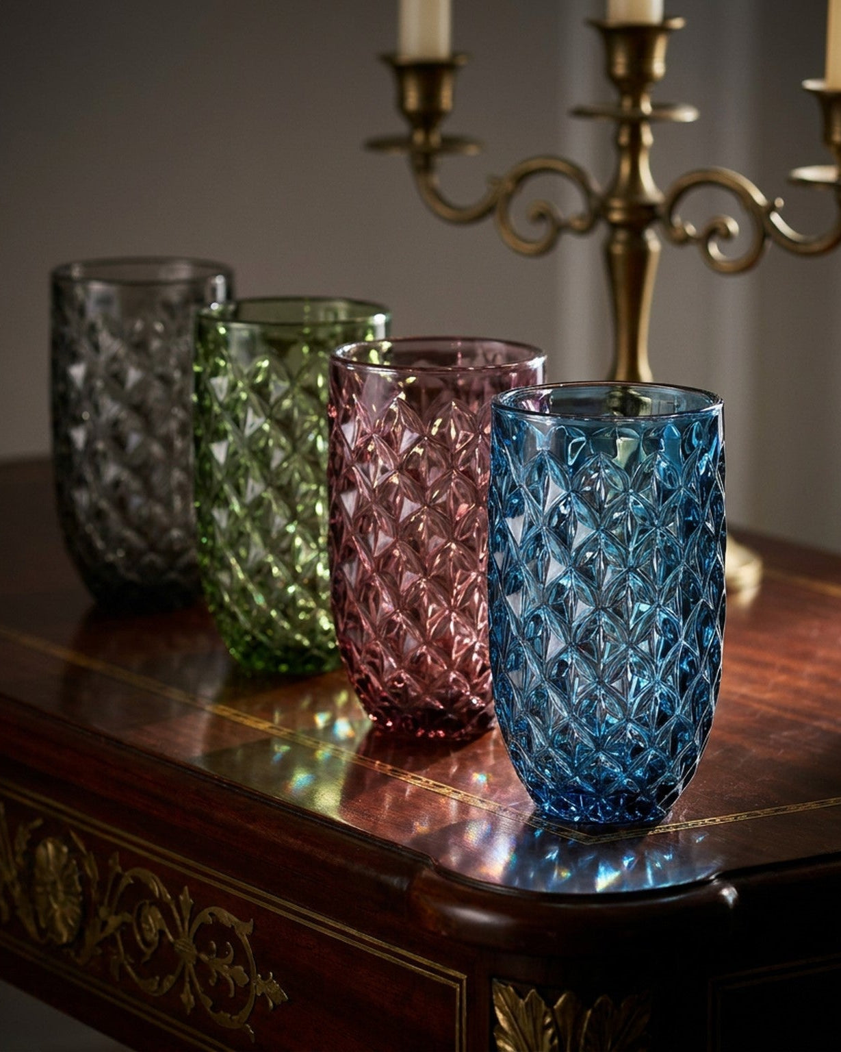 Four textured glass tumblers in pink, green, blue, and clear on a wooden surface.