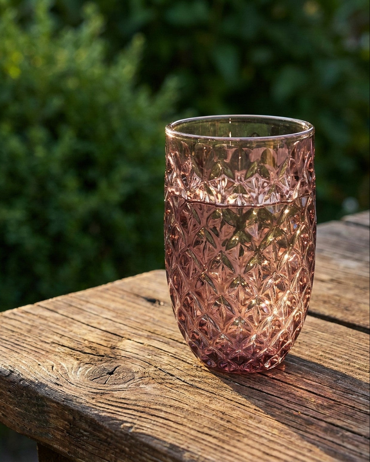 Set of pink glass tumblers on a wooden surface with a blue candle holder.