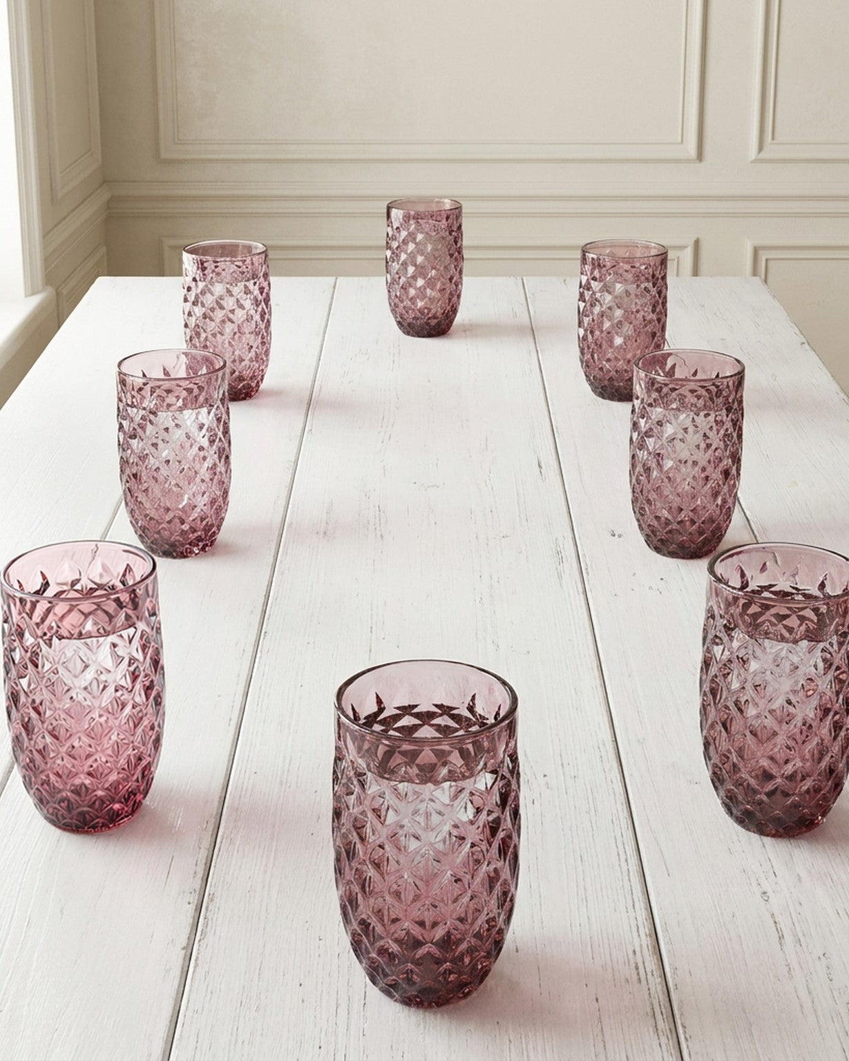 Pink textured glass tumblers on a wooden surface with a blue candle holder.