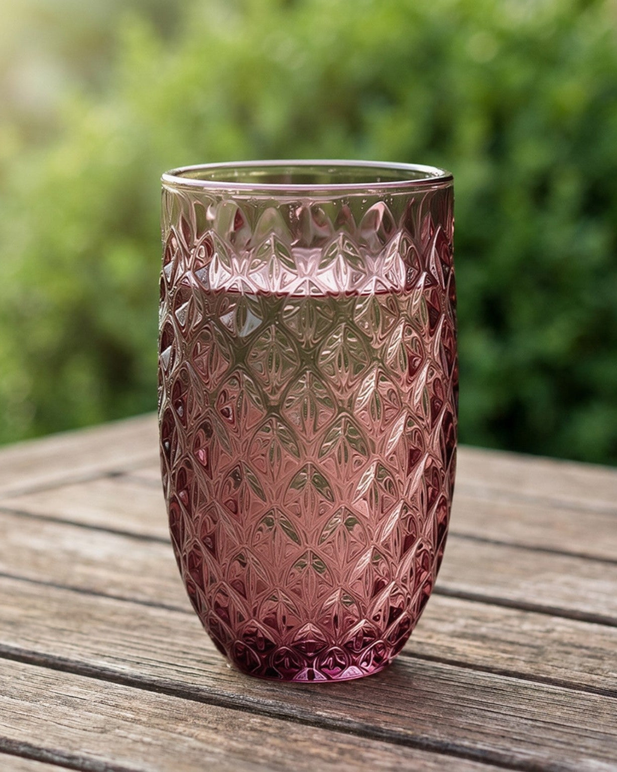 Set of pink glass tumblers on a wooden surface with a blue candle holder.