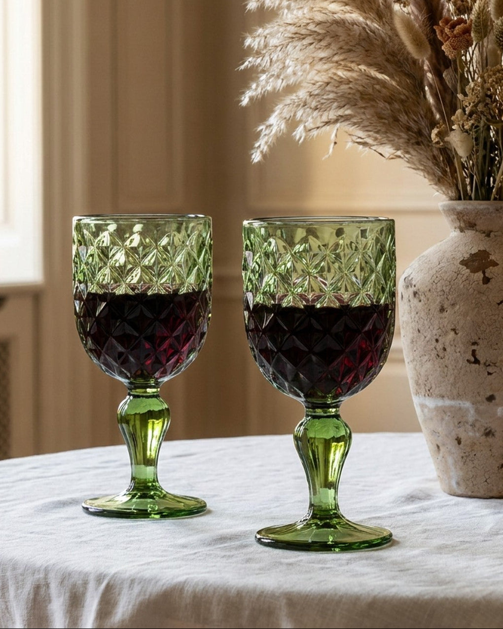 Set of green glass goblets on a marble surface with a sprig of eucalyptus.